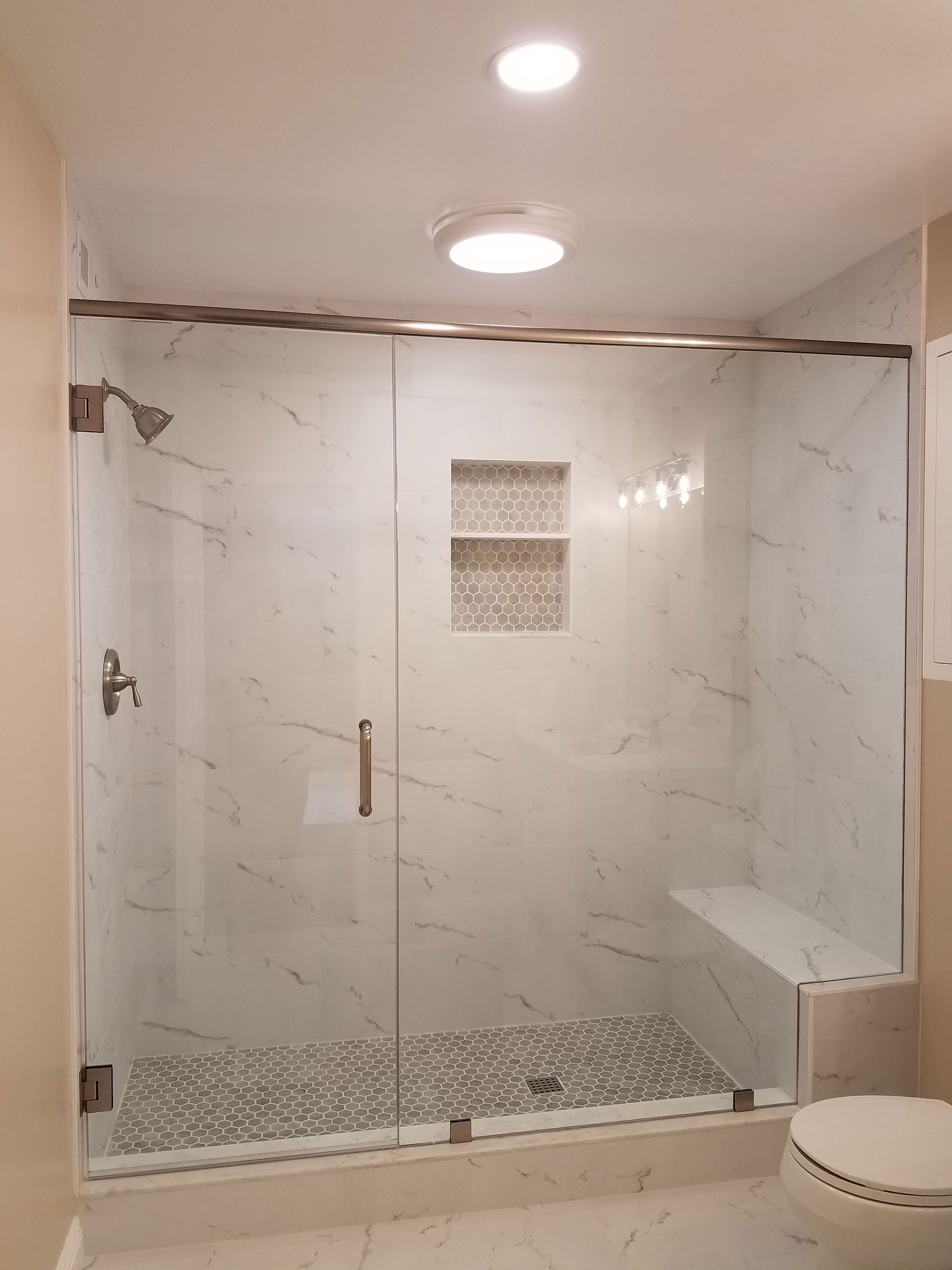 Modern white-tiled walk-in shower with glass doors and pebble-floor accent bathroom.