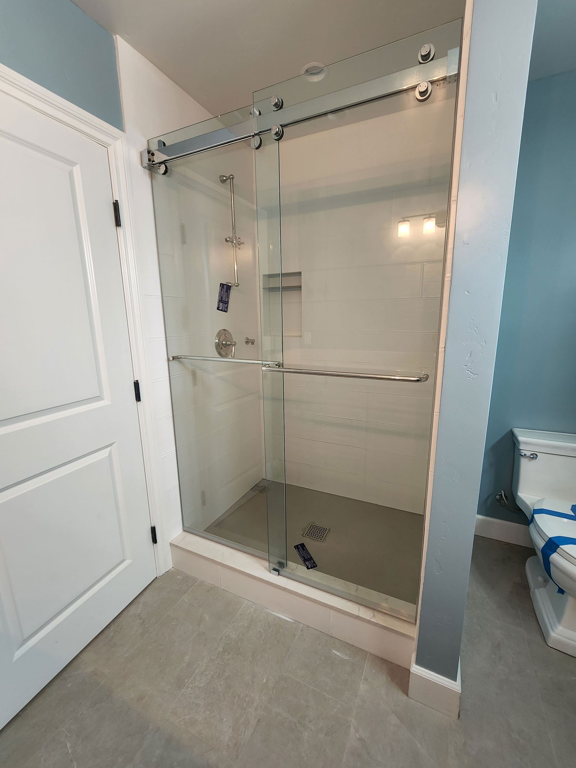 Bathroom shower stall with clear glass doors, chrome bar, and tiled walls in a light blue room