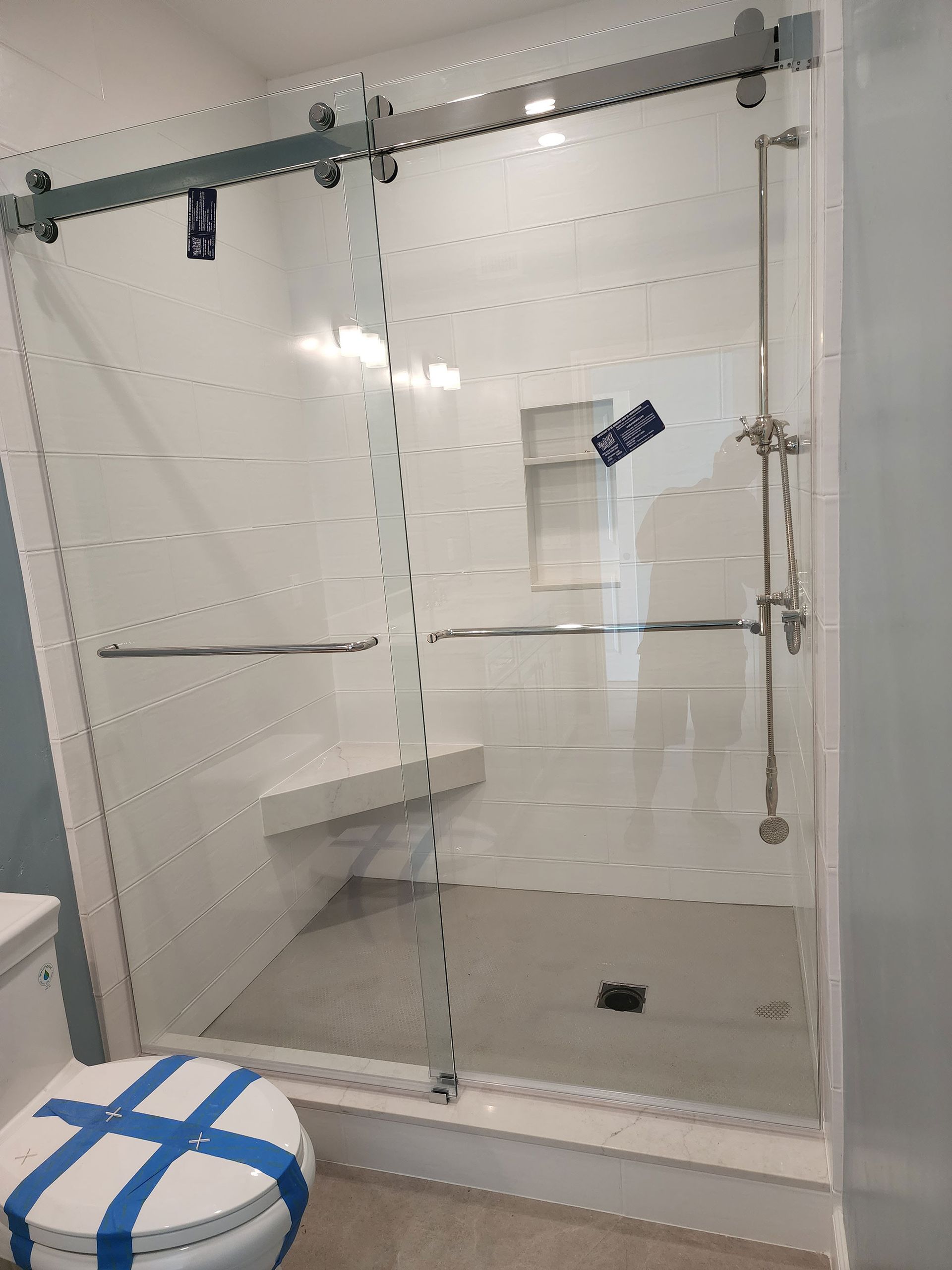 Glass shower with tiled bench and gray floor, viewed from outside; blue-and-white stool in foreground.