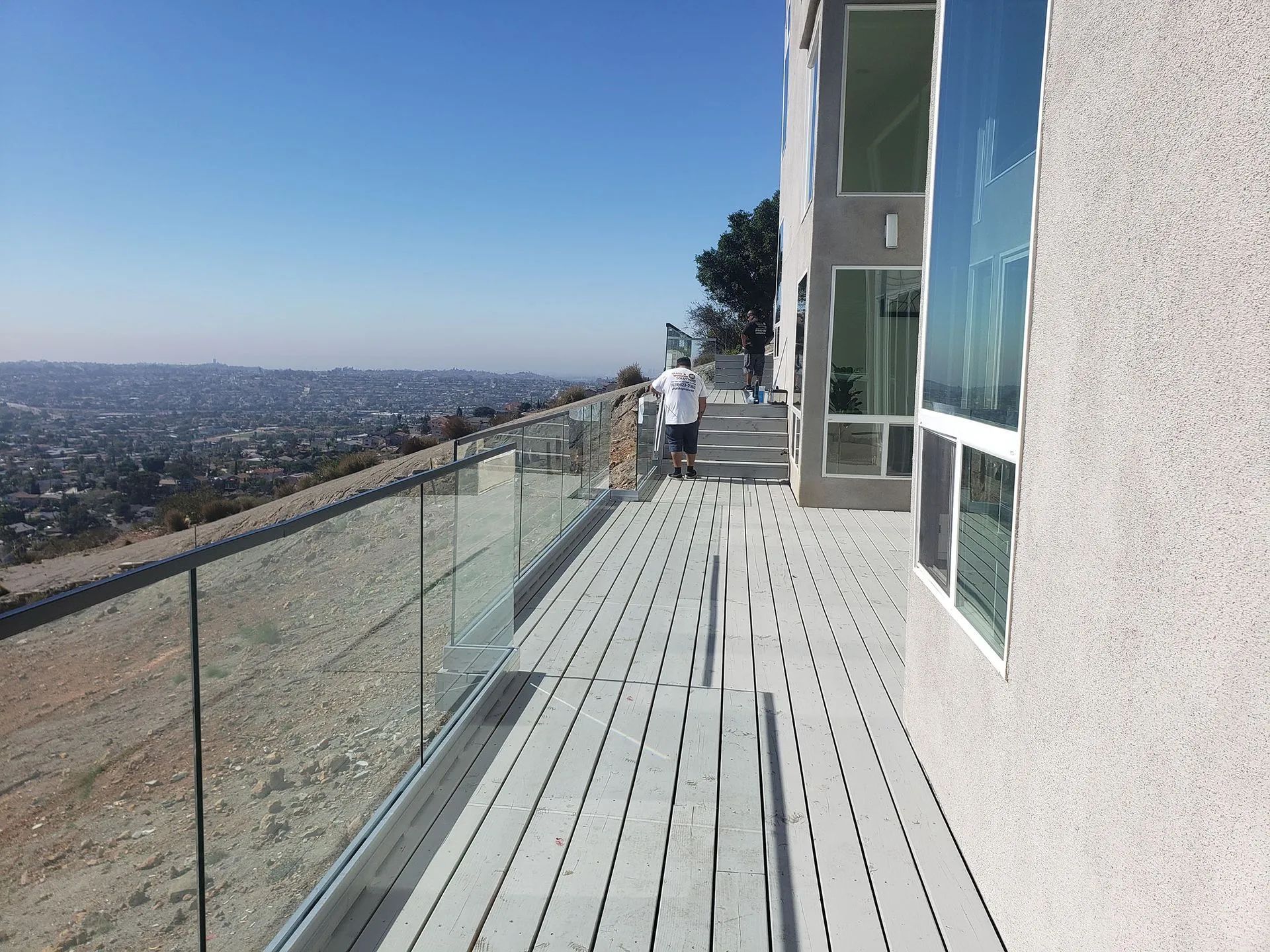 Sunny rooftop balcony with glass railing, city view, and a person standing near the edge
