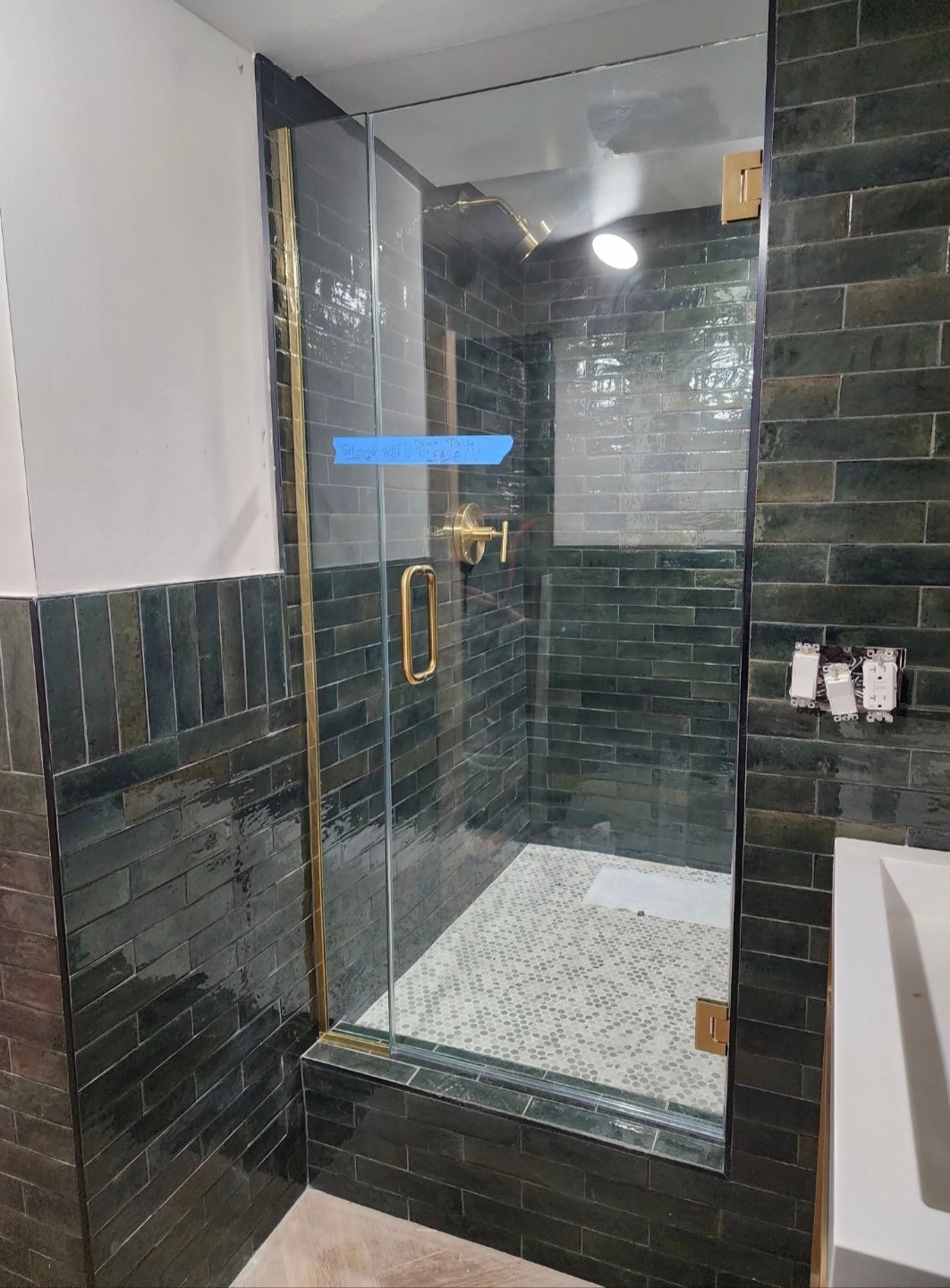 Glass shower enclosure in a dark-tiled bathroom with brass handle and white shower tray.