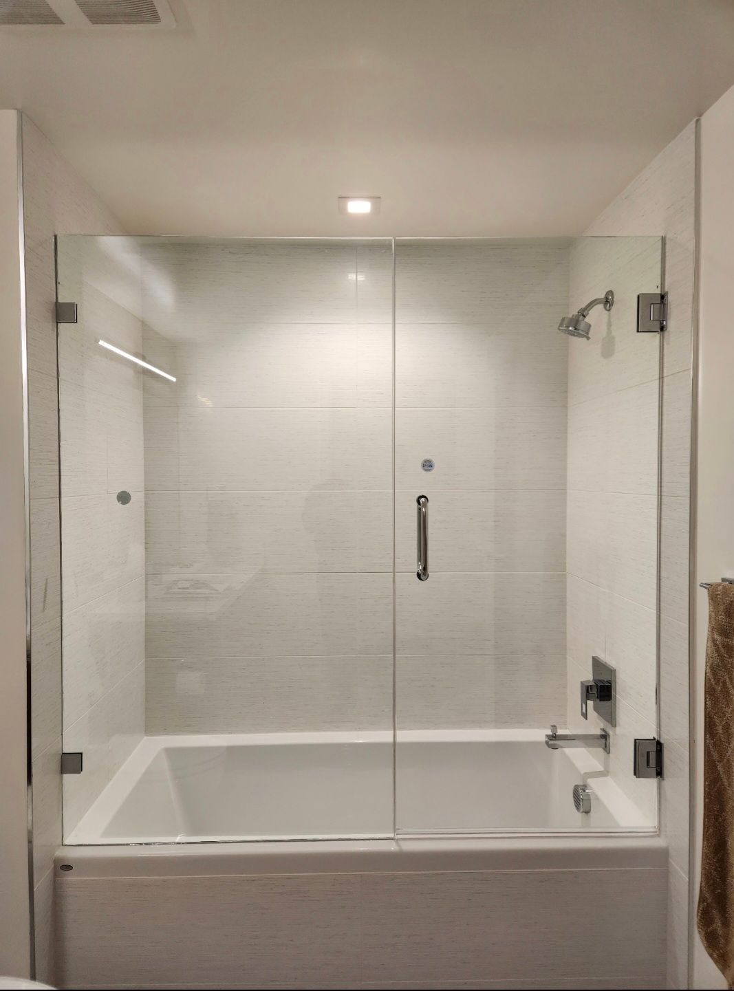 Bathroom with a glass-enclosed bathtub shower, white tile walls, and a chrome handle.