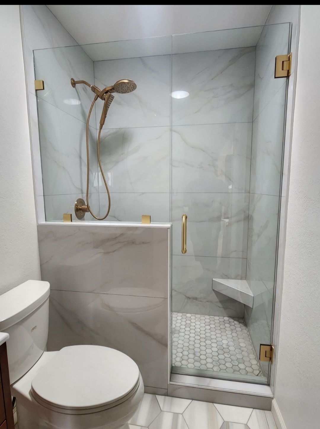 Compact bathroom with marble walls, glass shower, toilet, and shower fixtures.