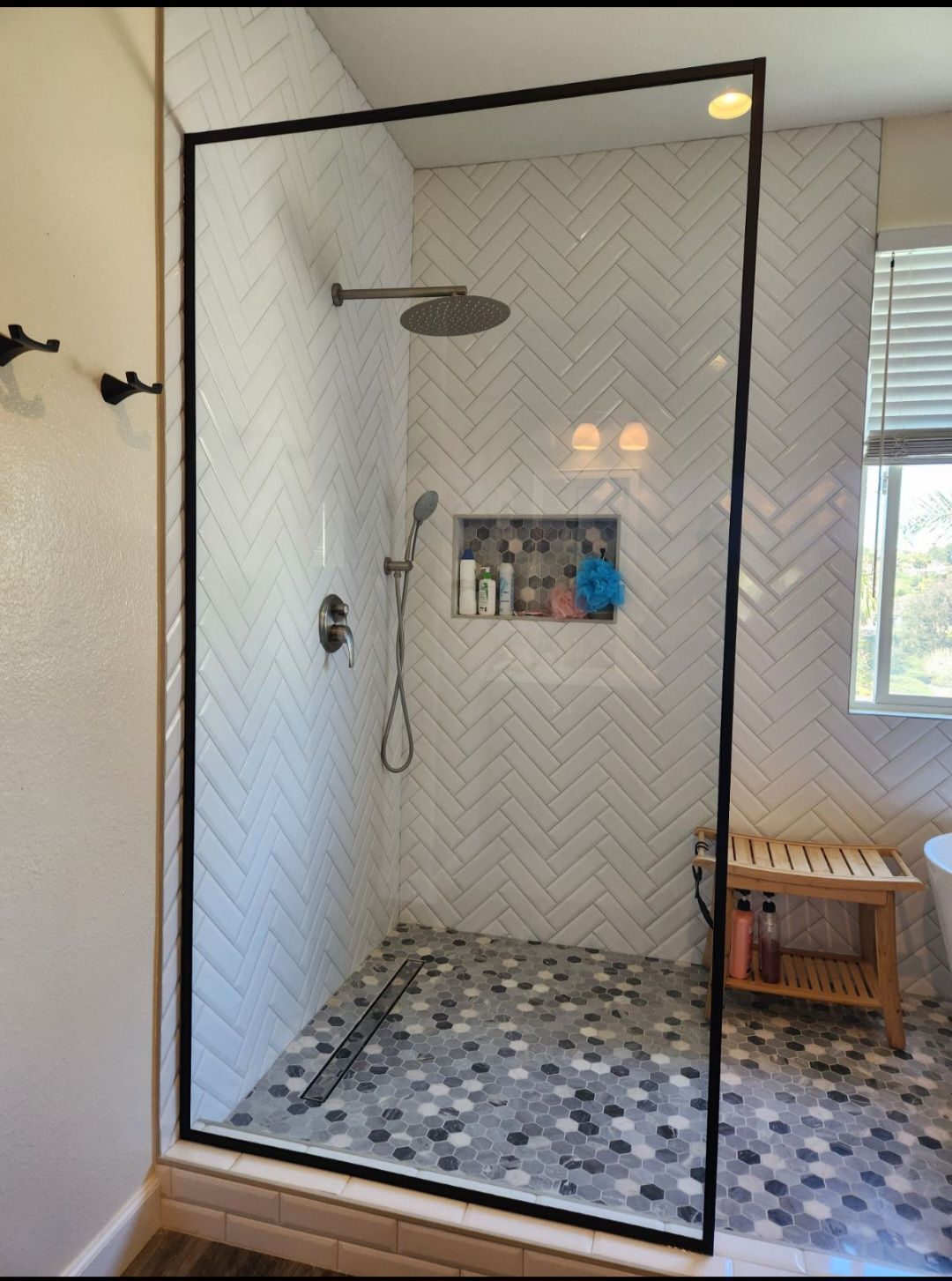 Frameless glass shower with black trim, patterned tile floor, and built-in shelf in a bright bathroom