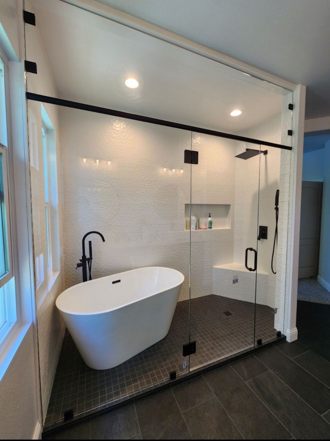 Modern bathroom with a freestanding white tub, black fixtures, and glass shower enclosure