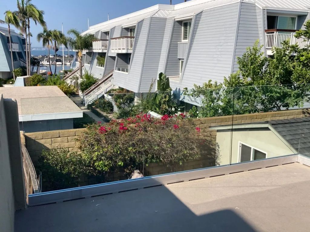 Balcony view of white condo buildings, palm trees, and flowering shrubs near the water.