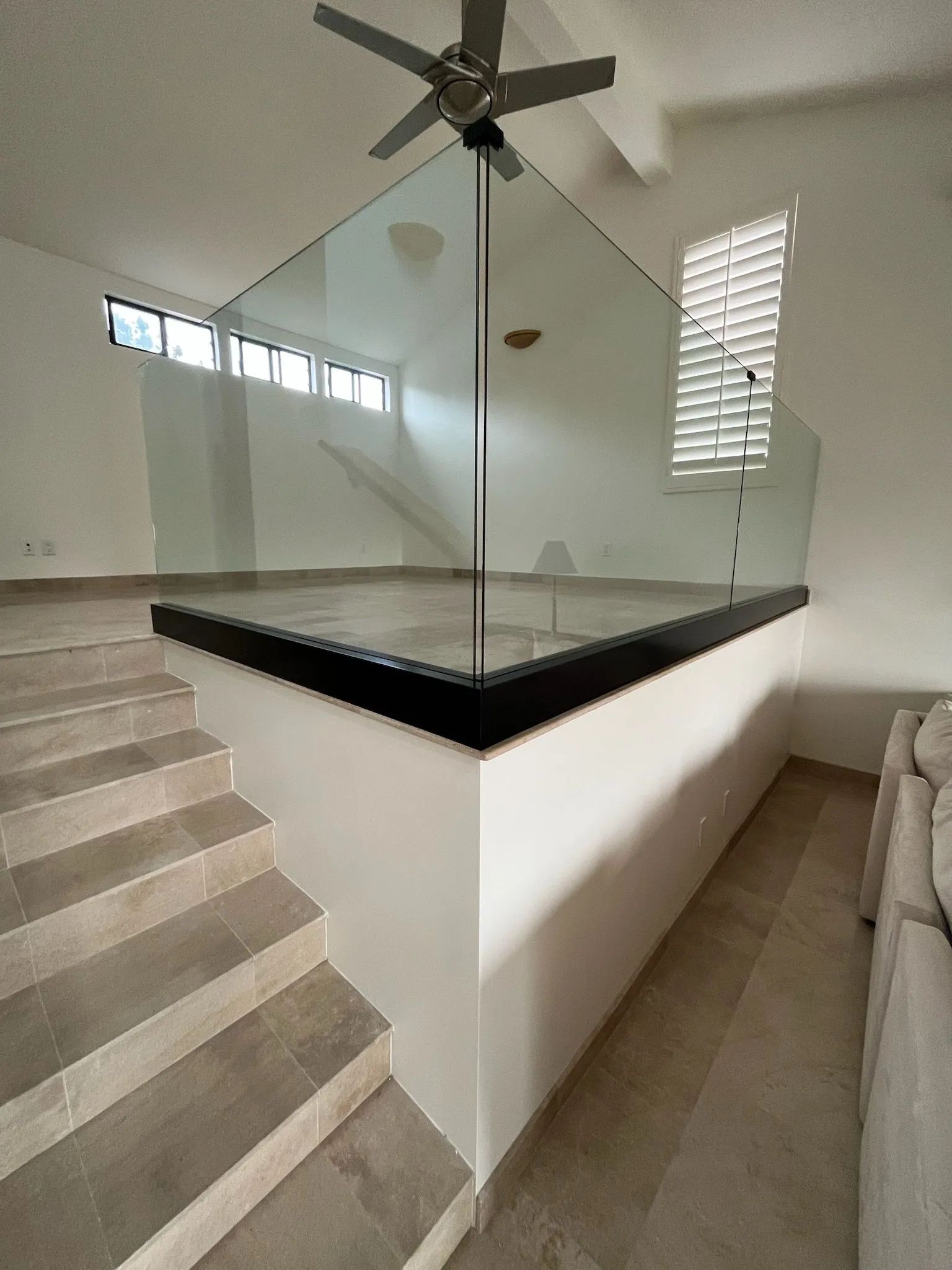 Modern stairwell with glass railing around a central landing and ceiling fan.