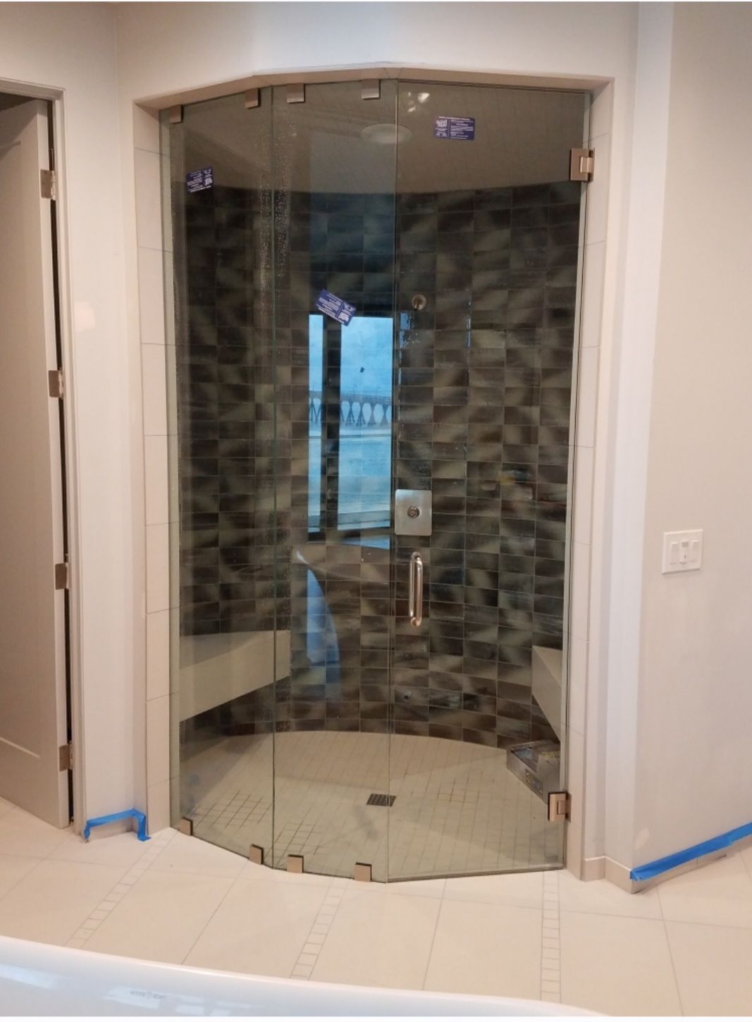 Curved glass shower enclosure with tiled walls and a bench in a bathroom