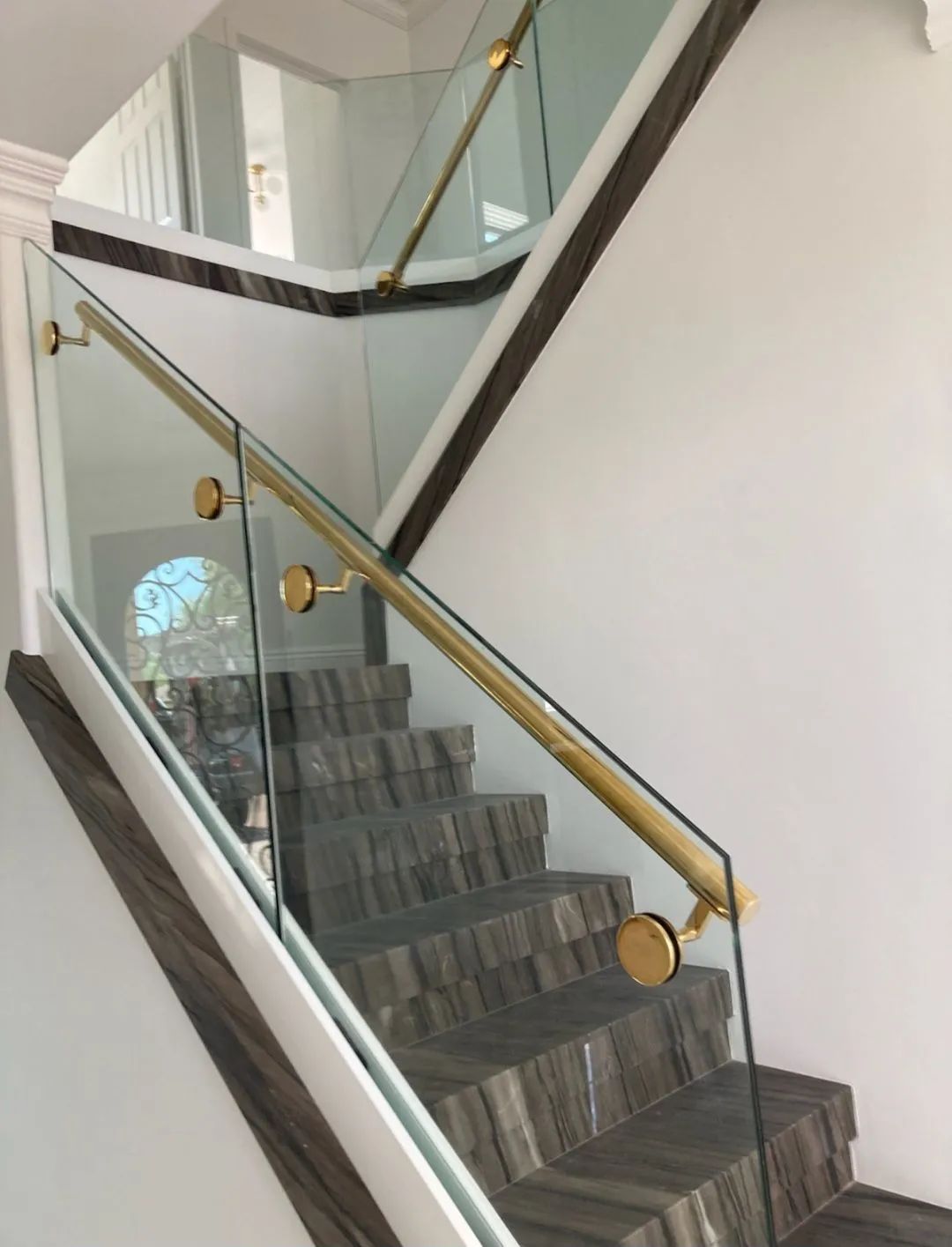 Modern indoor staircase with glass balustrade and brass handrail in a bright foyer