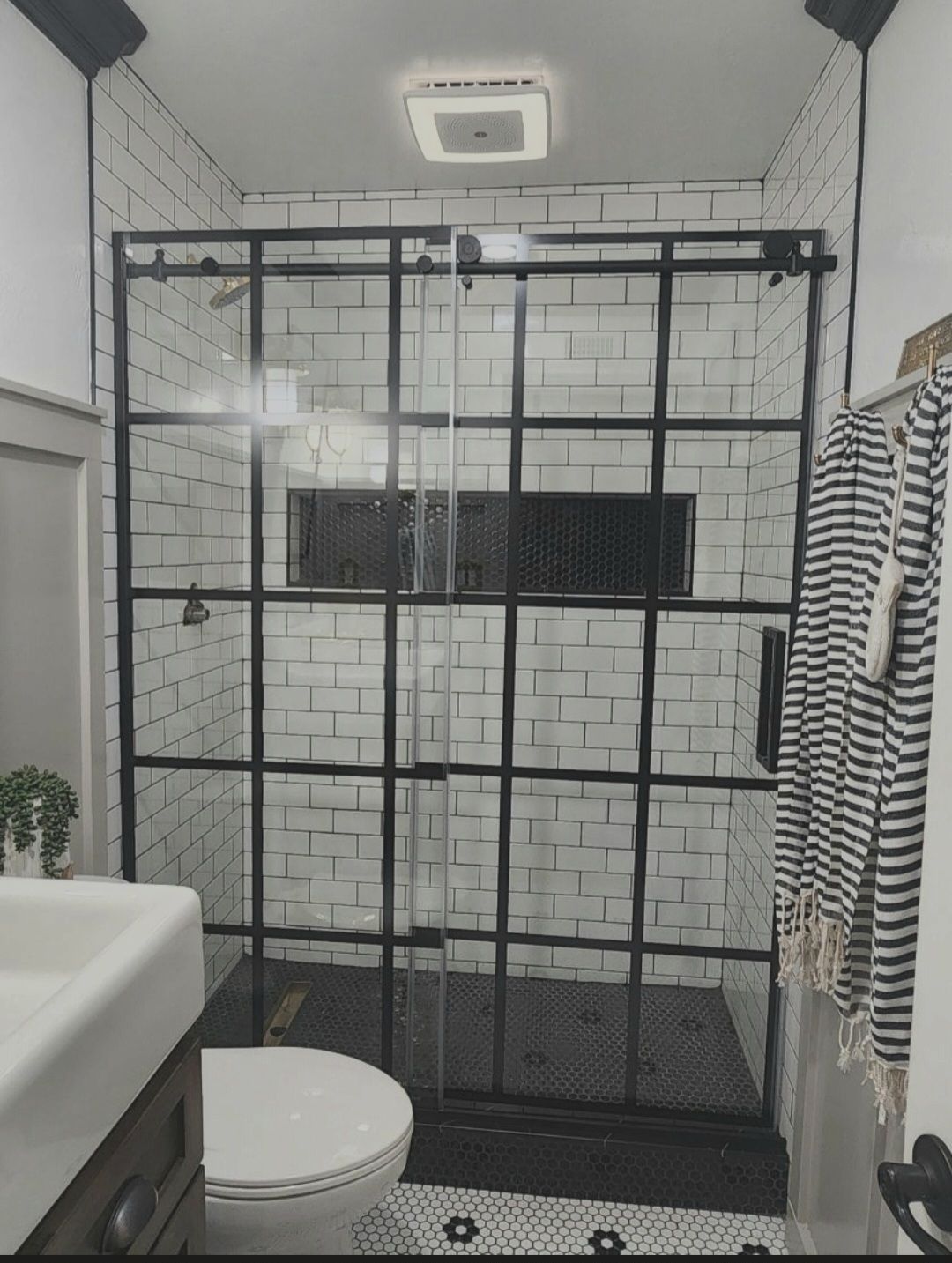Black shower enclosure in a white tiled bathroom with toilet, sink, and striped towel