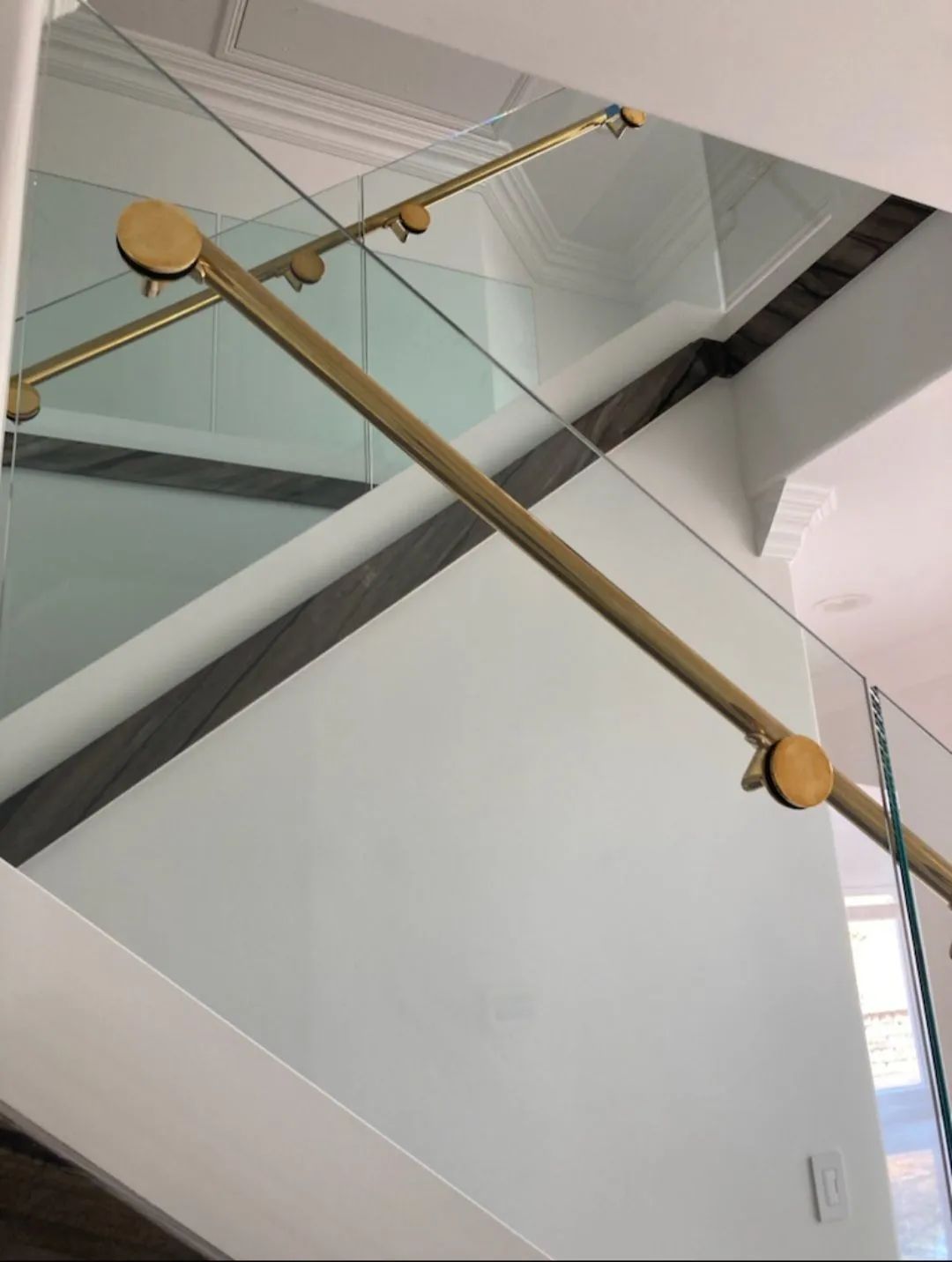 Glass staircase railing with gold handrails on a white interior landing