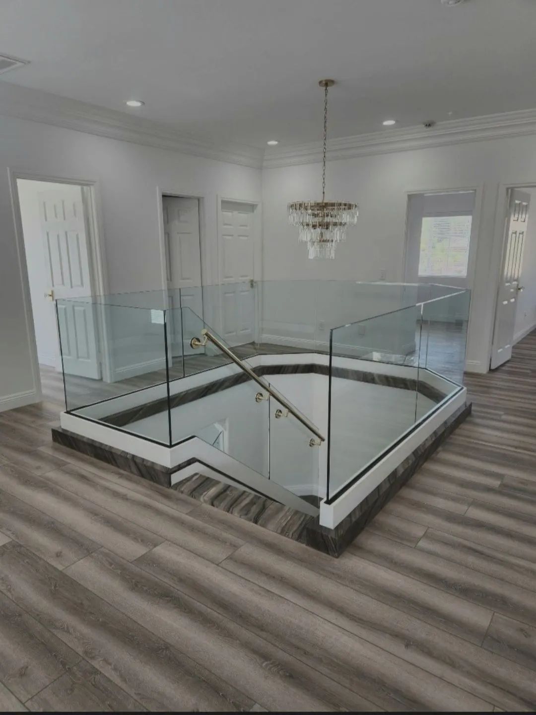 Modern foyer with glass stair railing, chandelier, gray walls, and wood-look flooring
