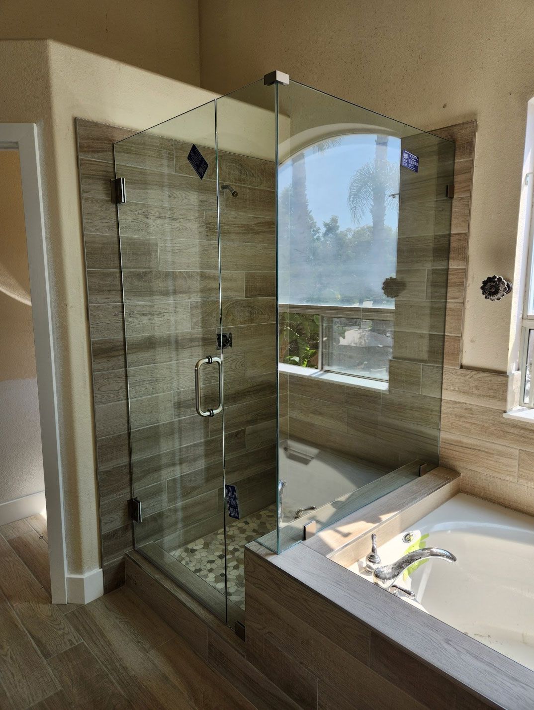 Modern bathroom with glass shower enclosure beside a large bathtub and window nook