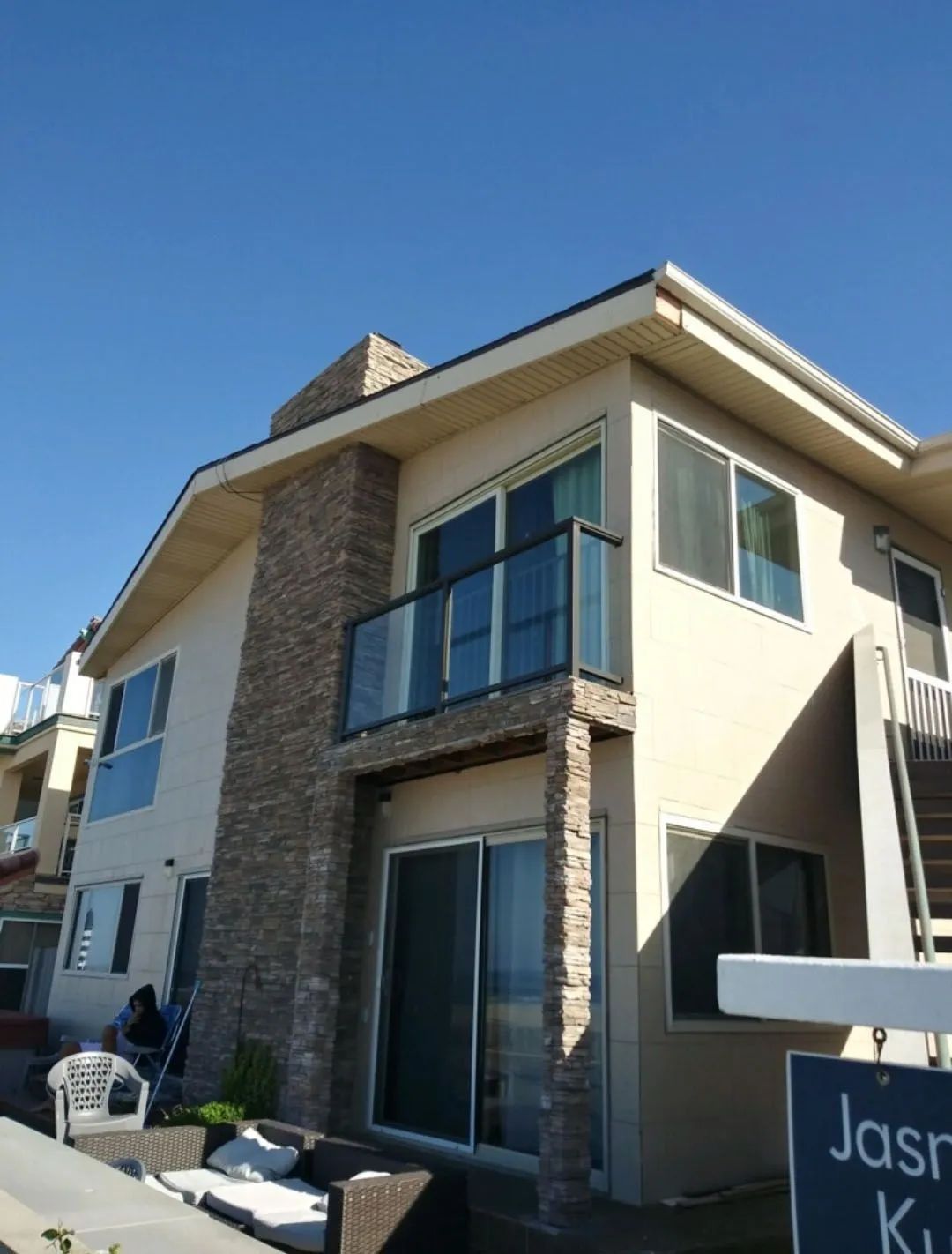 Modern beige two-story house with stone accents, glass balcony, and blue sky