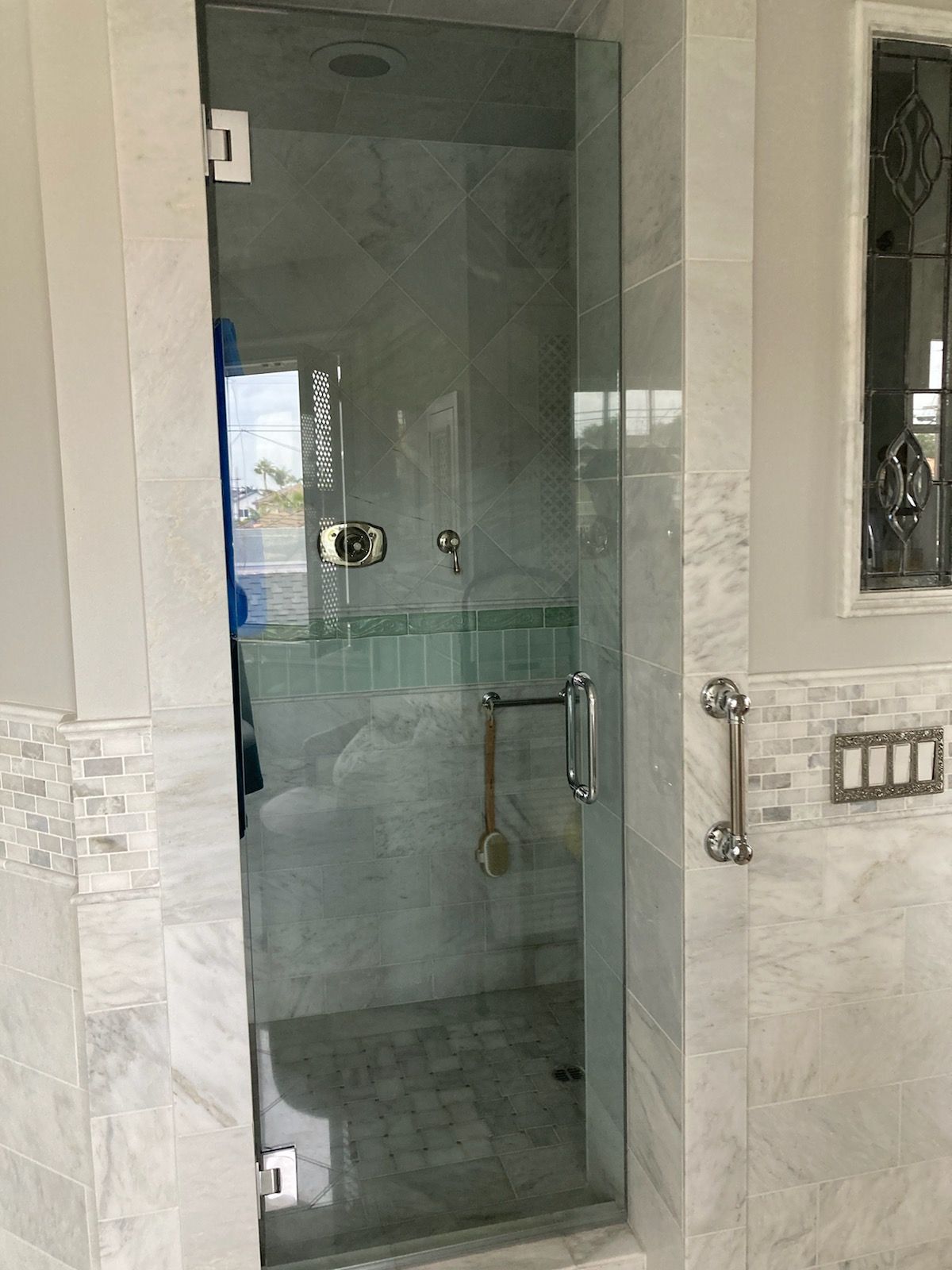 Glass shower enclosure with chrome handle in a white marble bathroom