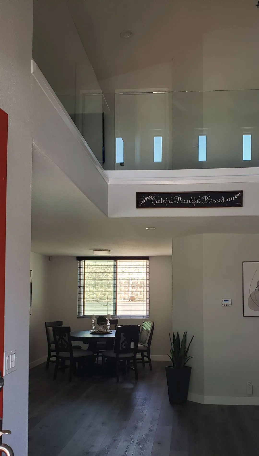 Bright living room with high ceilings, dining table, large window, and a potted plant near the entryway