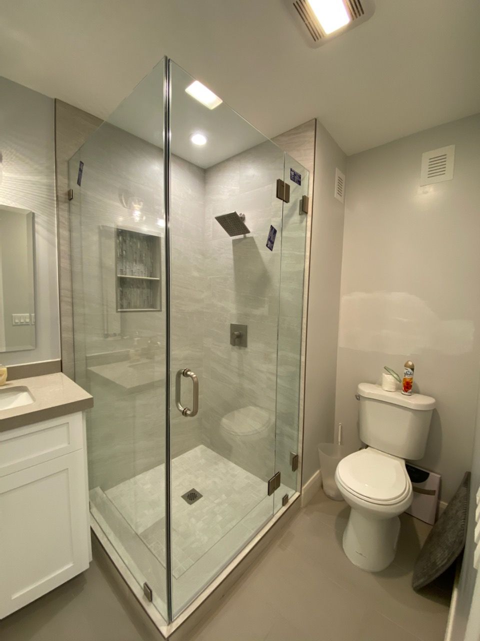 Modern bathroom with glass shower, white vanity, toilet, and beige tile walls