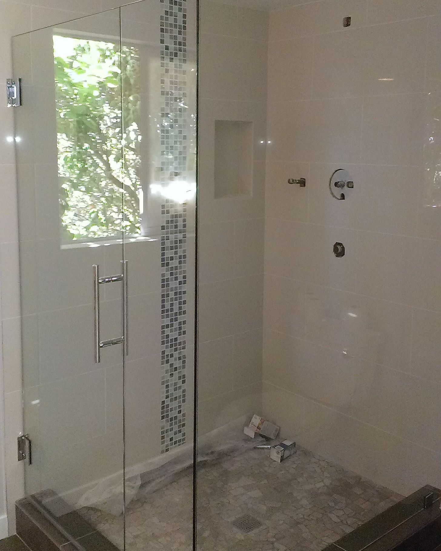 Modern walk-in shower with glass door, tiled walls, and a small window.