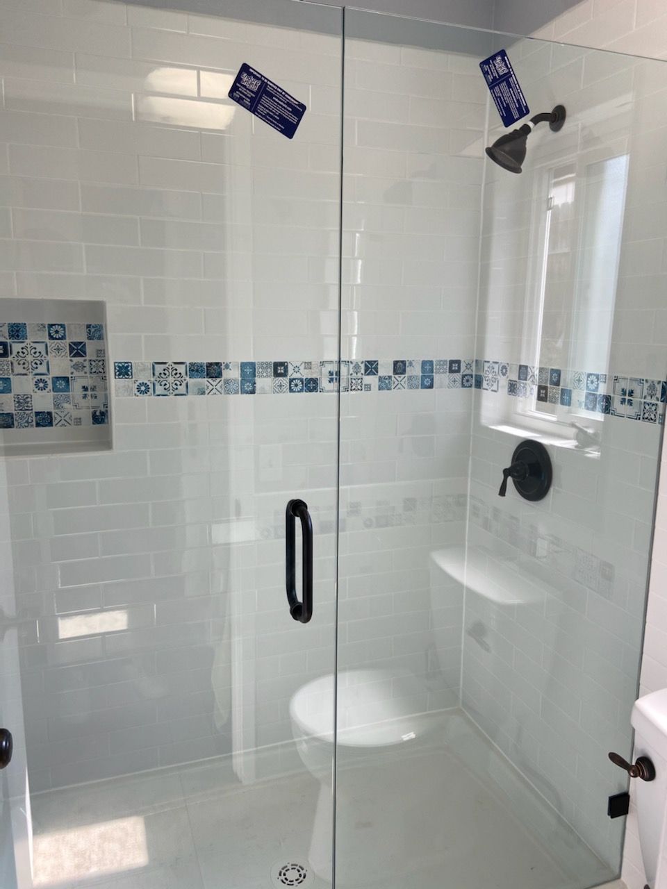 Glass shower enclosure in a bright bathroom with white tile and blue accent border.