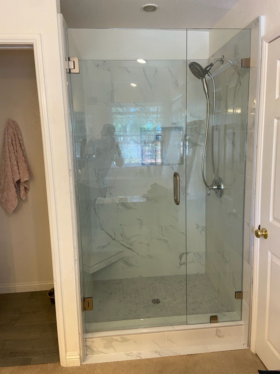 Glass-enclosed shower with marble walls and handheld showerhead in a bathroom doorway