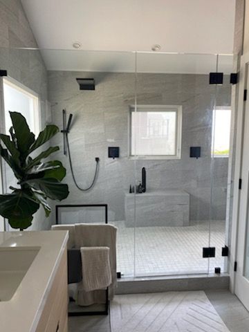 Modern bathroom with glass shower, white tile, freestanding tub, and a large plant by the window.