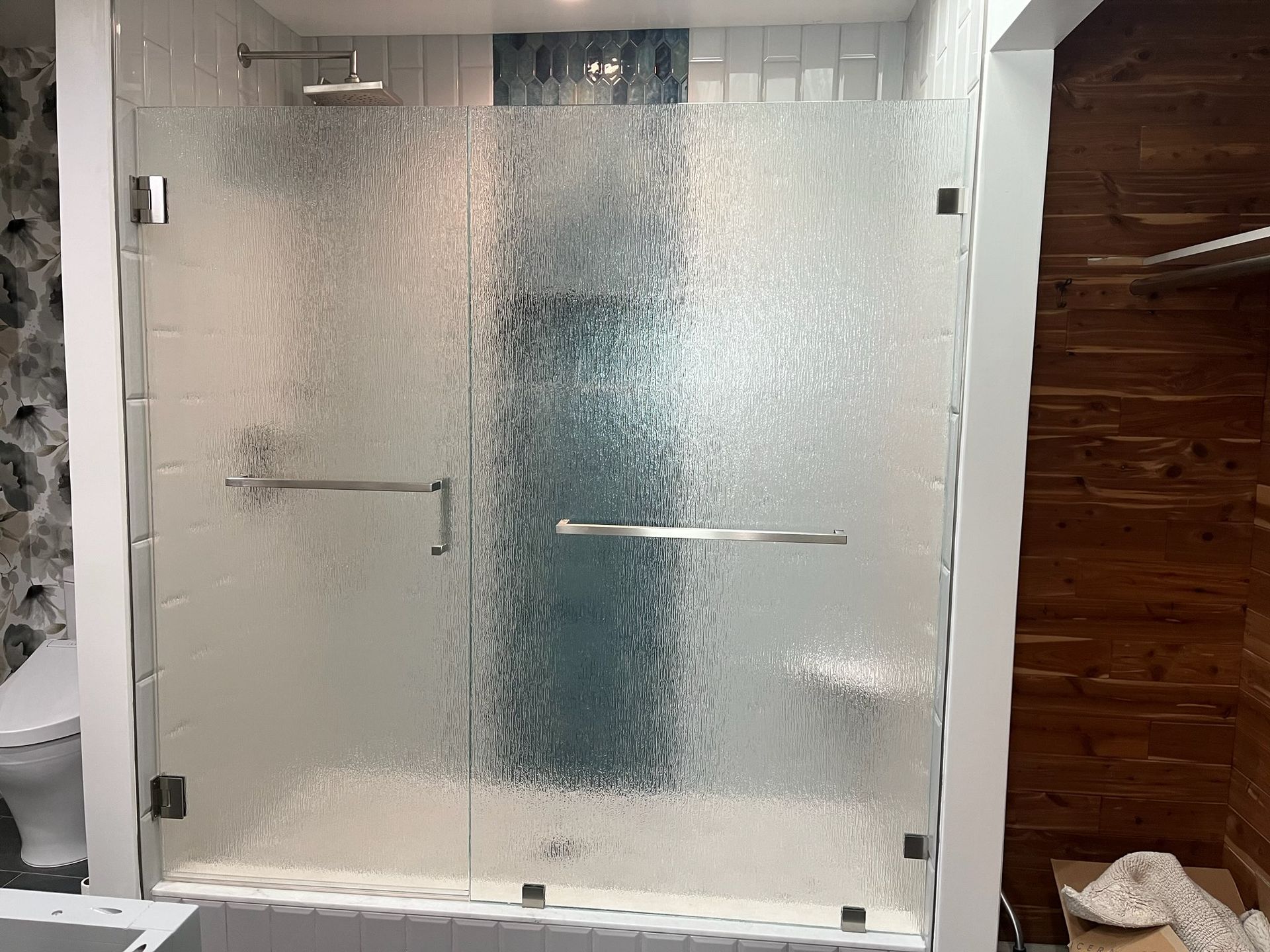 Frosted glass shower enclosure with chrome handles and white tile walls, beside a wood-paneled wall