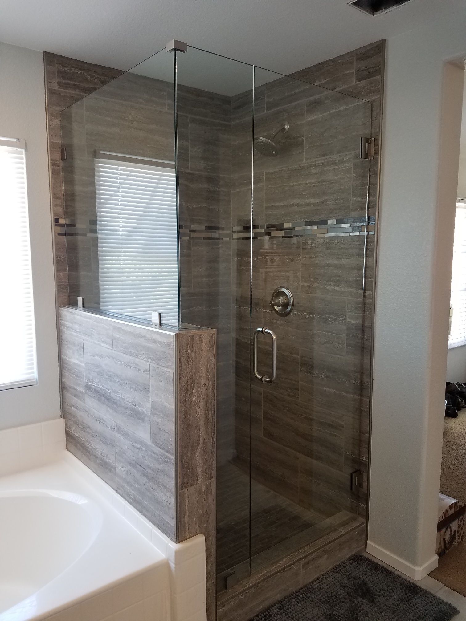 Modern bathroom with a glass-enclosed tiled shower and a white bathtub in the foreground