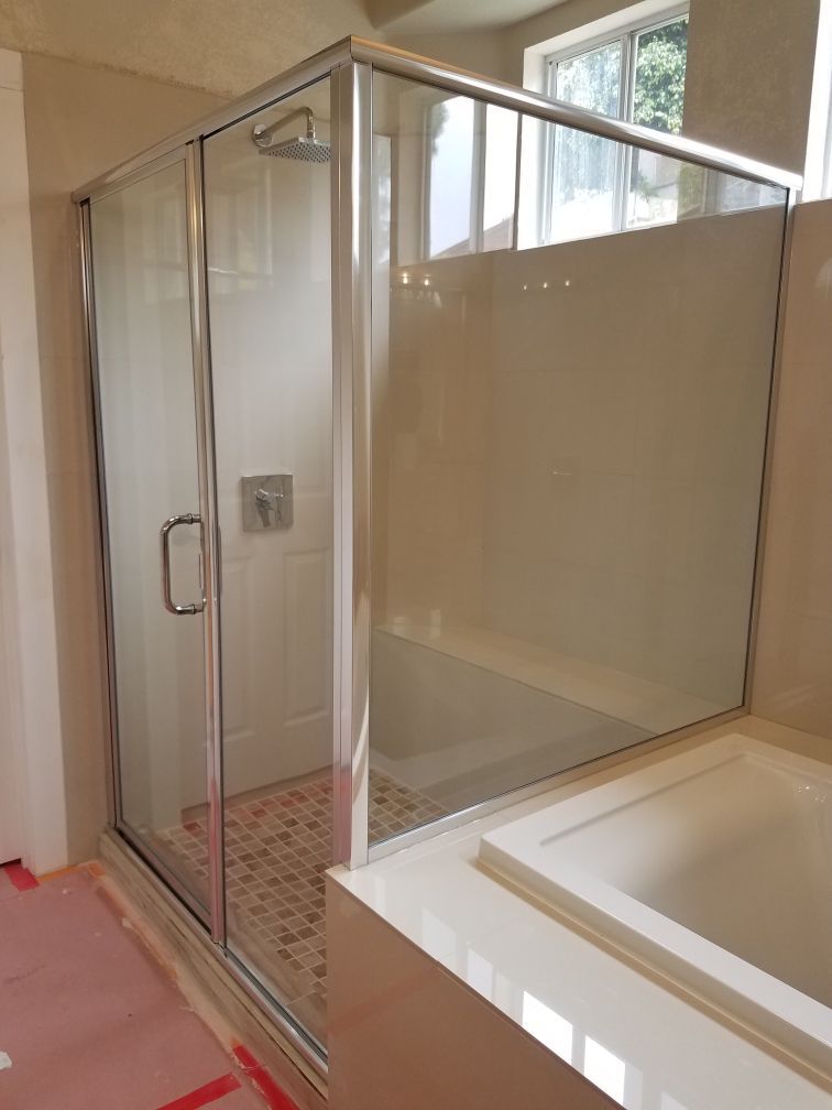 Bathroom with glass shower stall beside a white bathtub and pink tile floor, lit by a window.