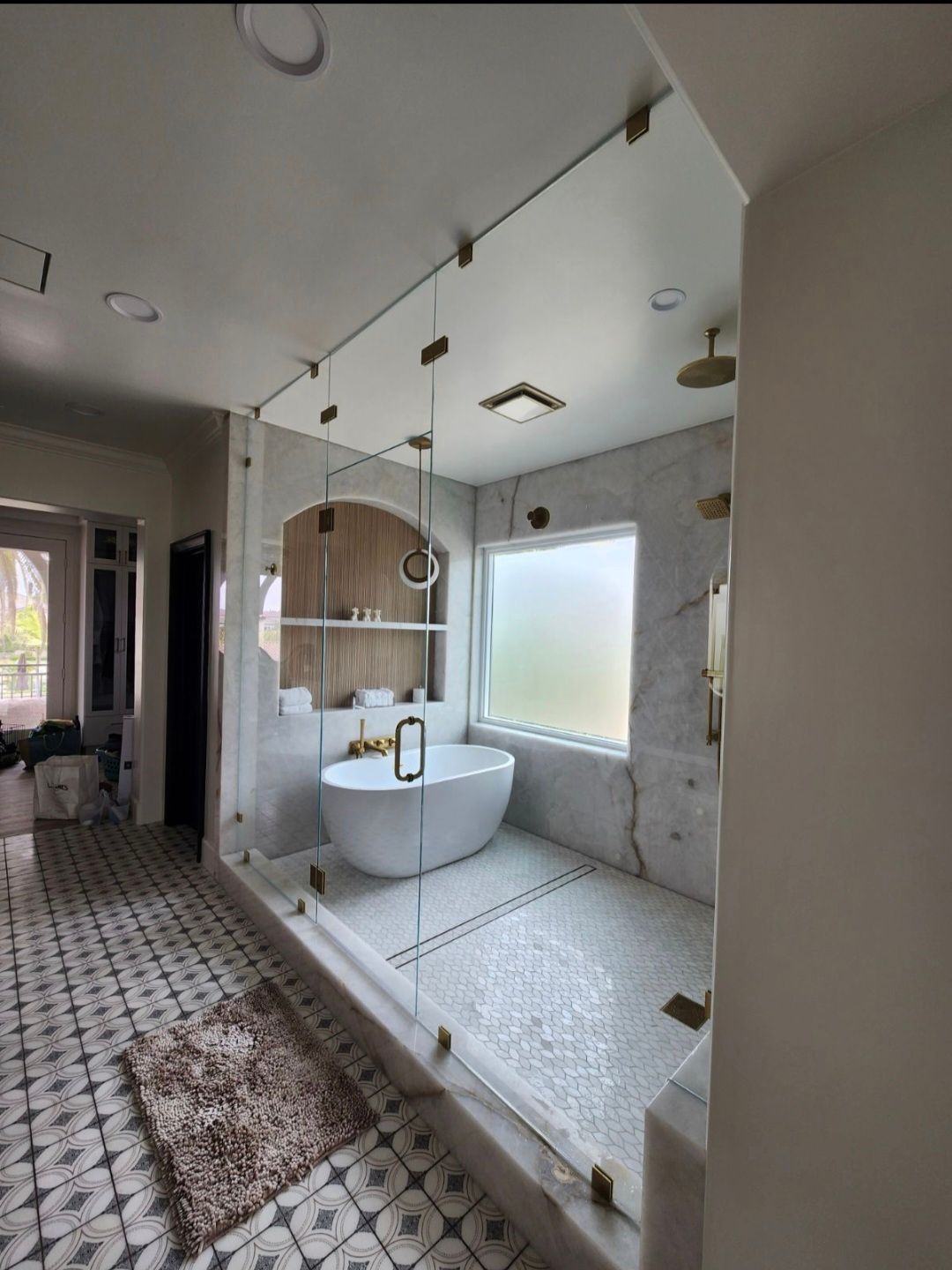 Bright tiled bathroom with walk-in shower, freestanding tub, large mirror, and frosted window.