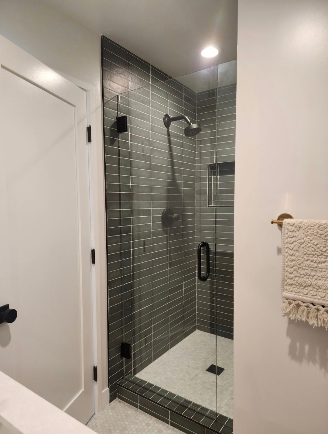 Glass-tiled walk-in shower with black fixtures and white bathroom walls