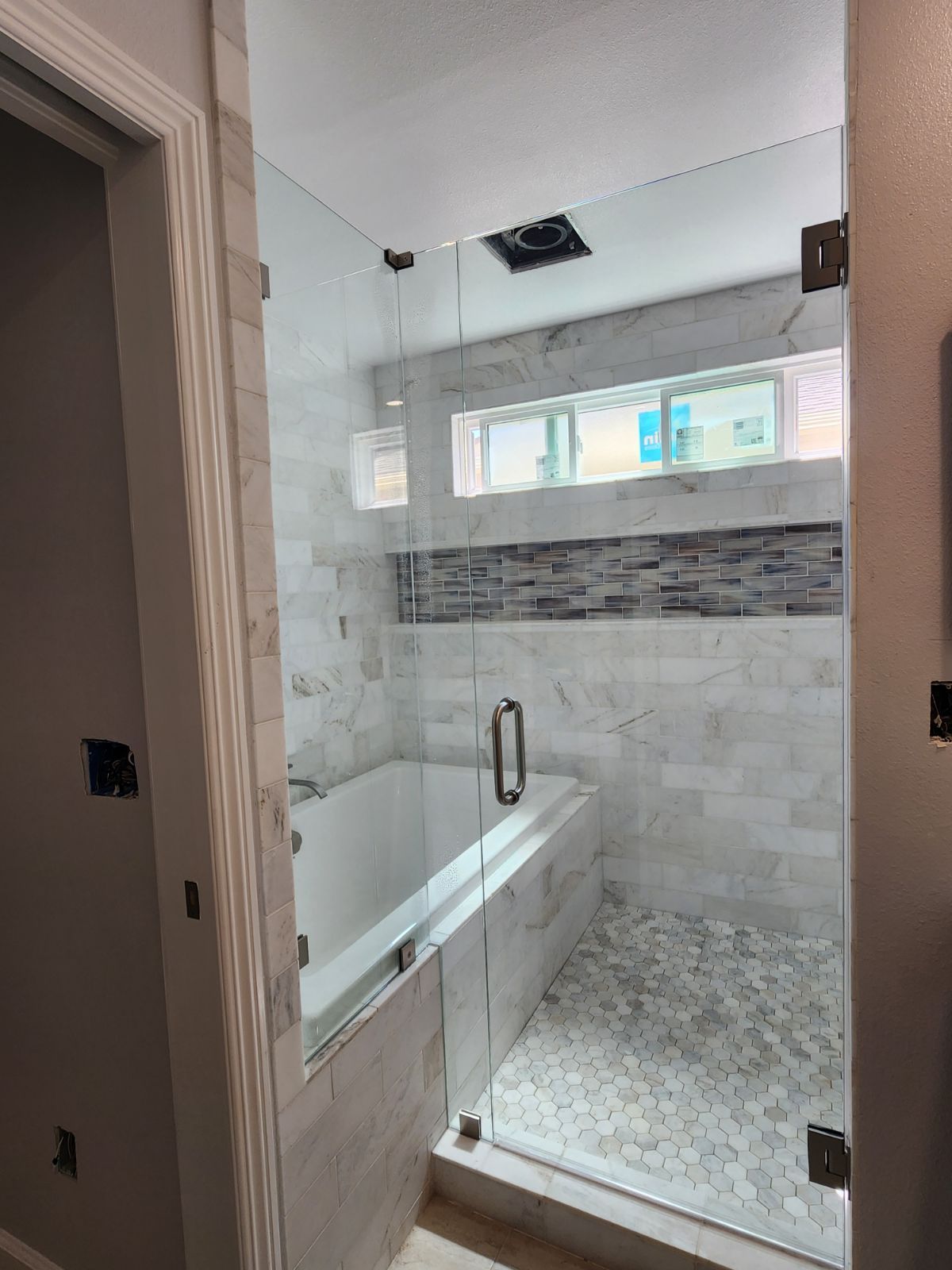 Modern tiled bathroom with a bathtub, glass shower enclosure, and small horizontal window.