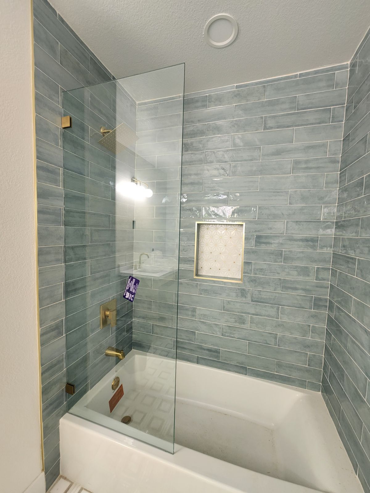 Modern bathroom with a glass-enclosed bathtub, blue tile walls, and a recessed wall niche.