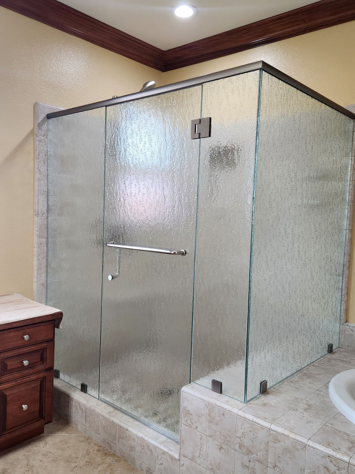 Glass walk-in shower enclosure in a bathroom with beige tile and a white tub beside it