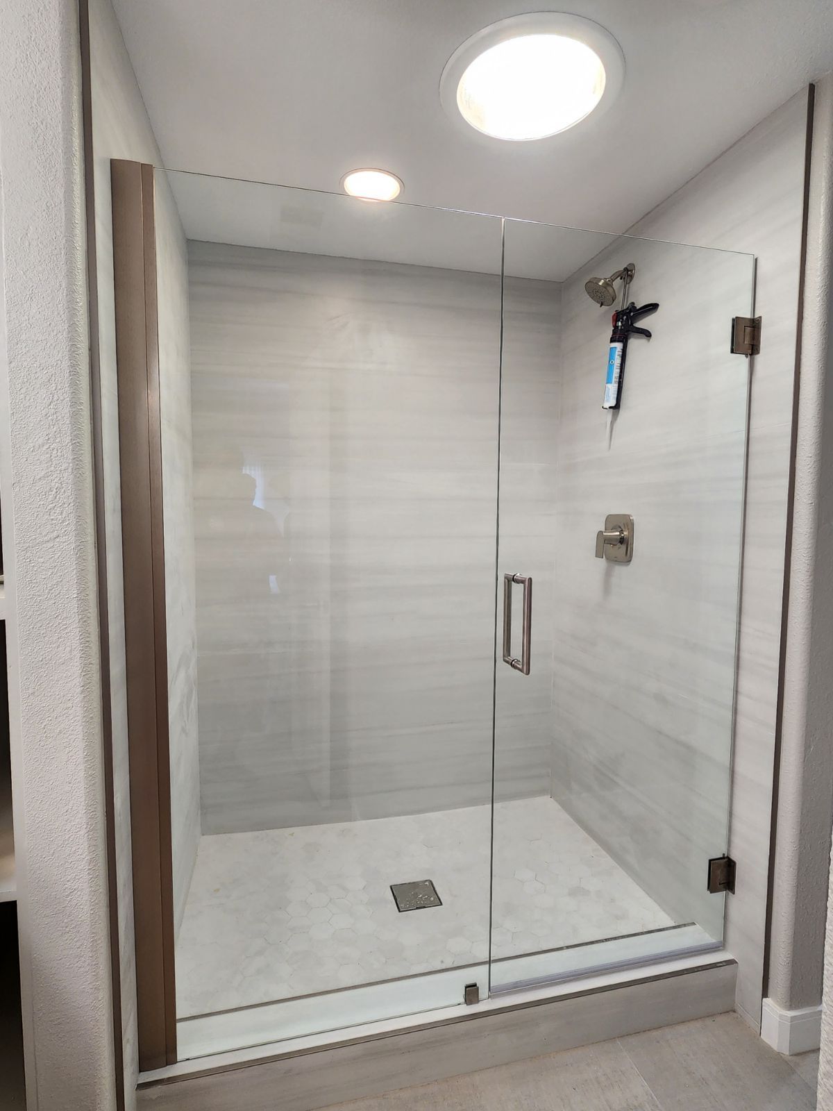 Modern glass shower enclosure with gray tile walls and a small floor drain in a bathroom