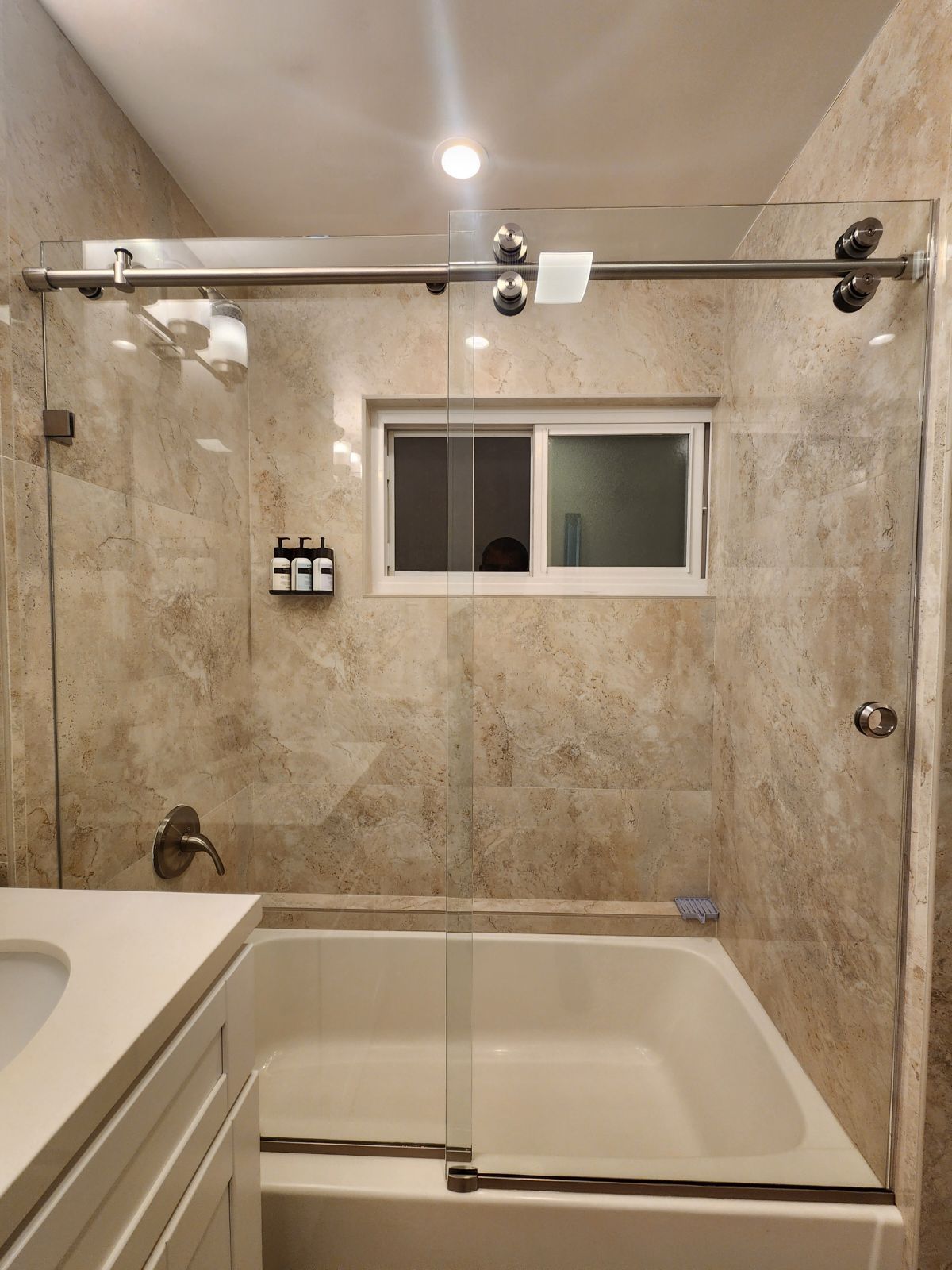 Bathroom with beige tile, a bathtub, shower bar, window, and vanity counter