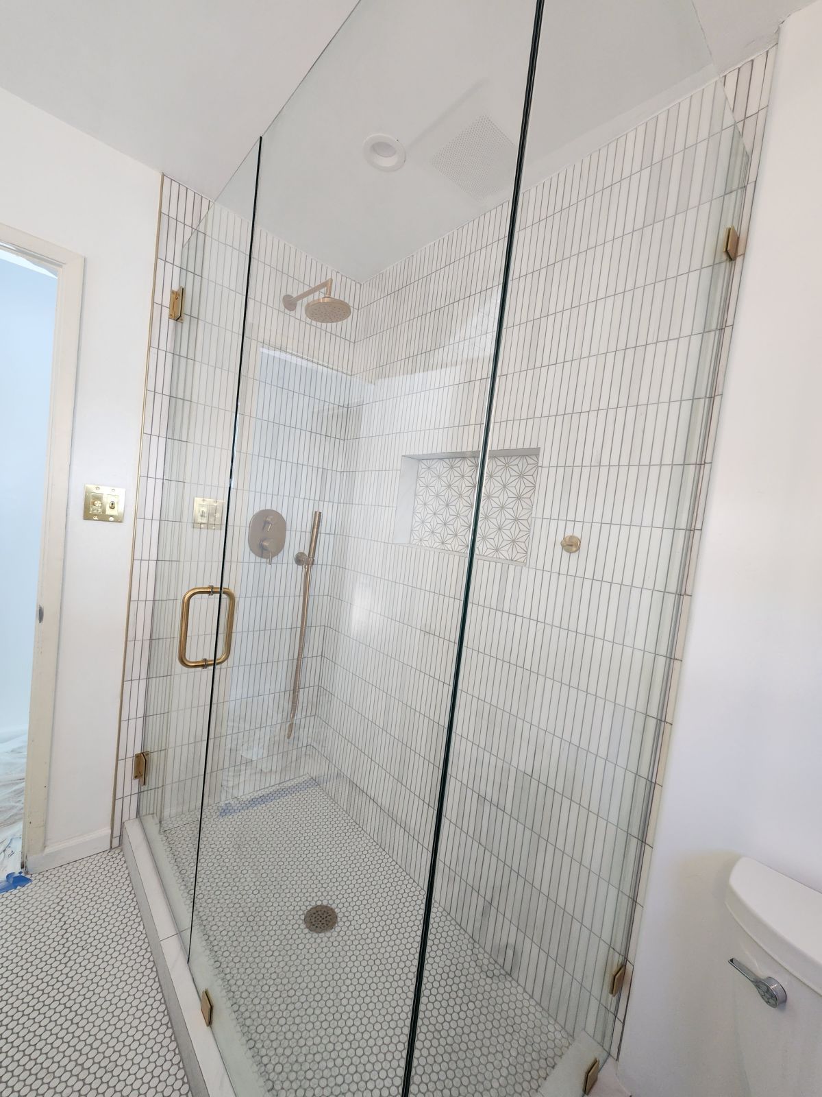 Walk-in shower with glass doors, white tile walls, and brass fixtures in a bright bathroom