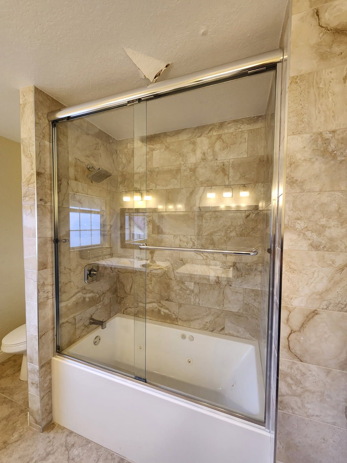 Marble-tiled bathroom with a glass-enclosed shower-tub combo and chrome fixtures