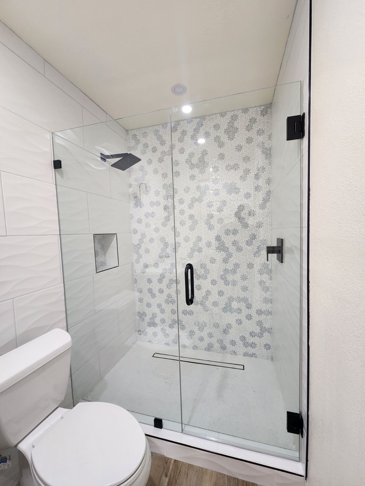 Modern white bathroom with walk-in glass shower and toilet, featuring patterned tile walls.