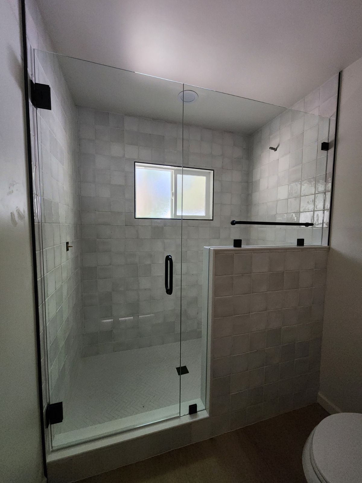 Modern bathroom with glass shower, tiled walls, and a small frosted window.