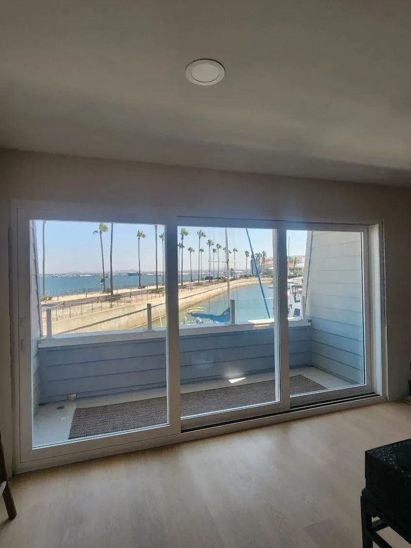 Bright balcony view through sliding glass doors, with ocean and promenade visible outside.