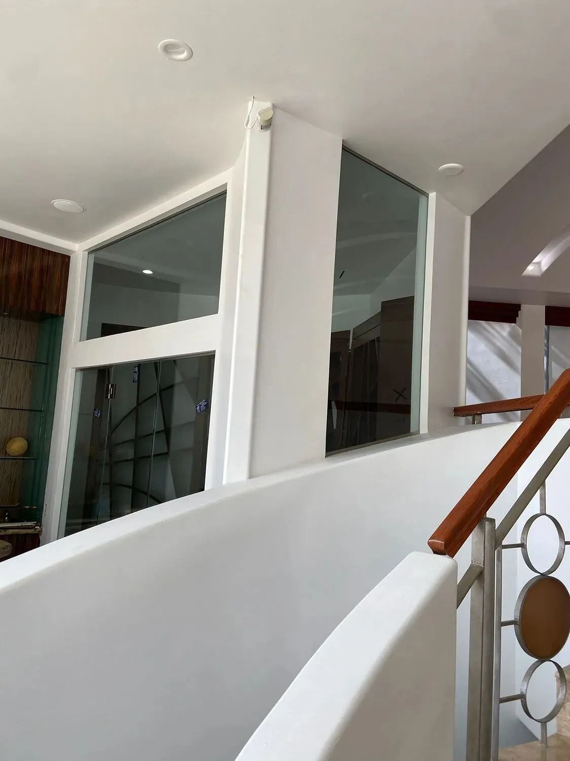 Interior staircase with white walls, glass panels, and a wooden handrail in a modern home