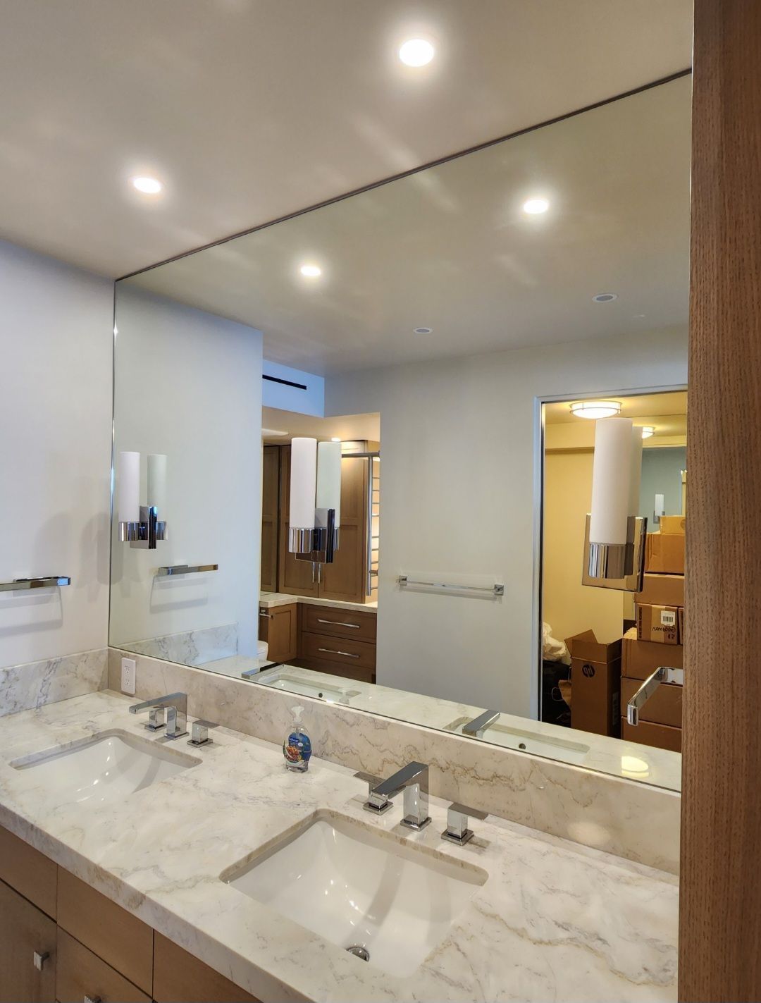Modern bathroom with double vanity, large mirror, and white marble countertop under recessed lights