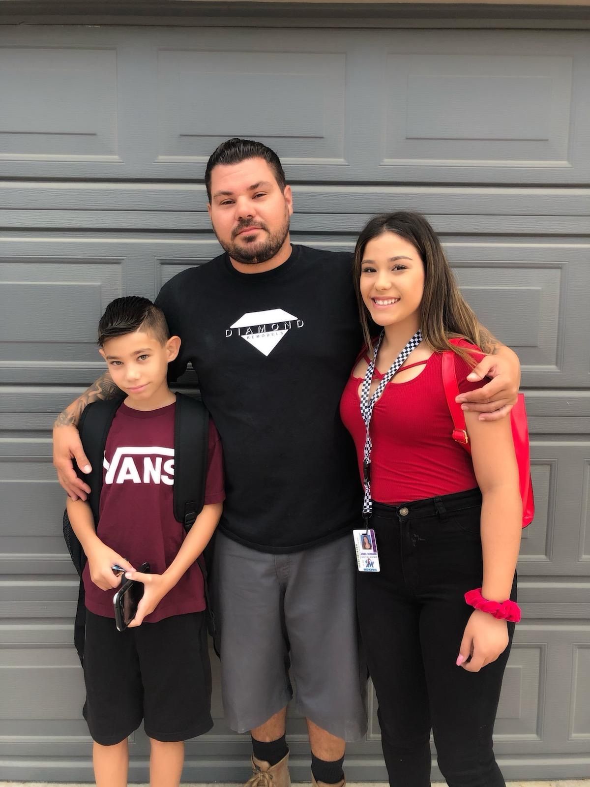Man with two children in front of a gray garage door. Son in Vans shirt, daughter in red top.