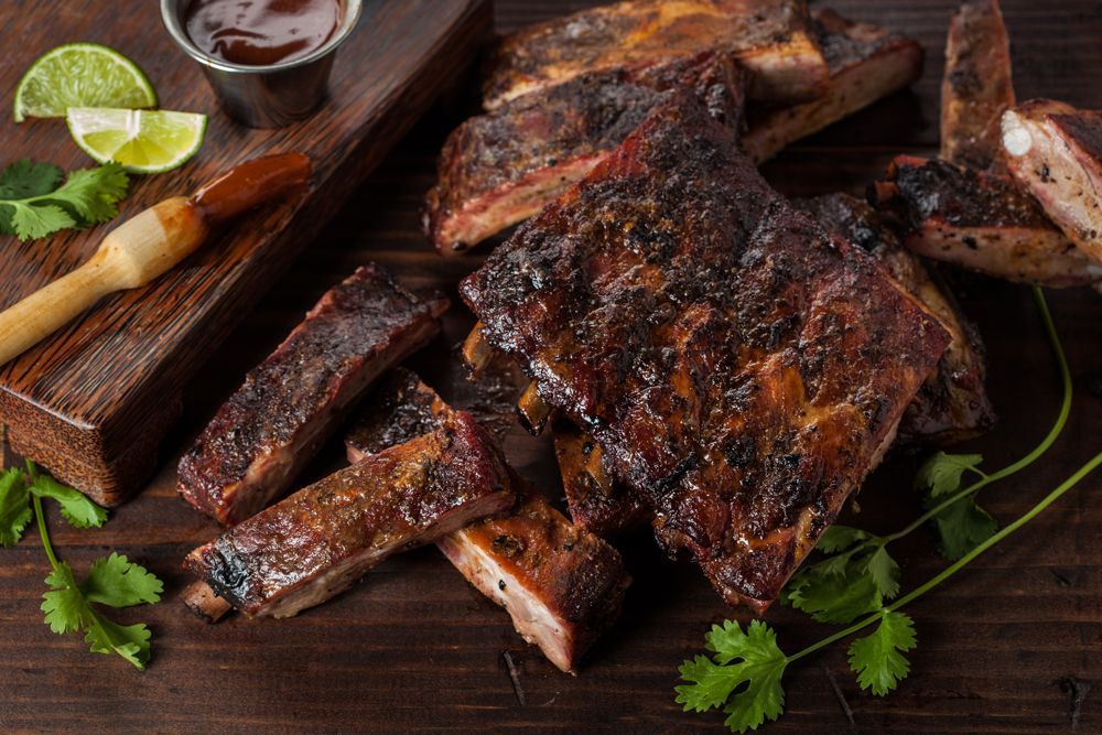 BBQ ribs on wooden board with sauce, limes, and cilantro.