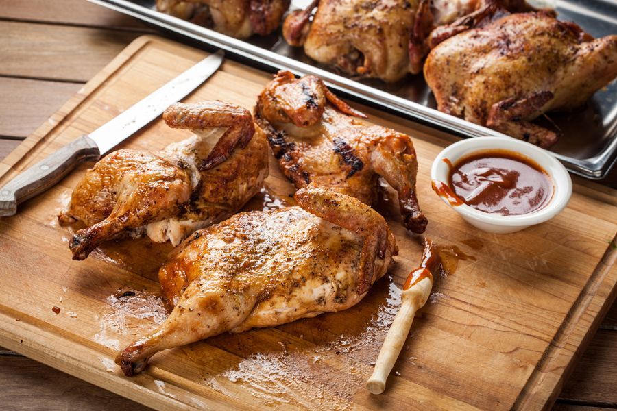 Roasted chicken pieces on a wooden board with dipping sauce and a knife.