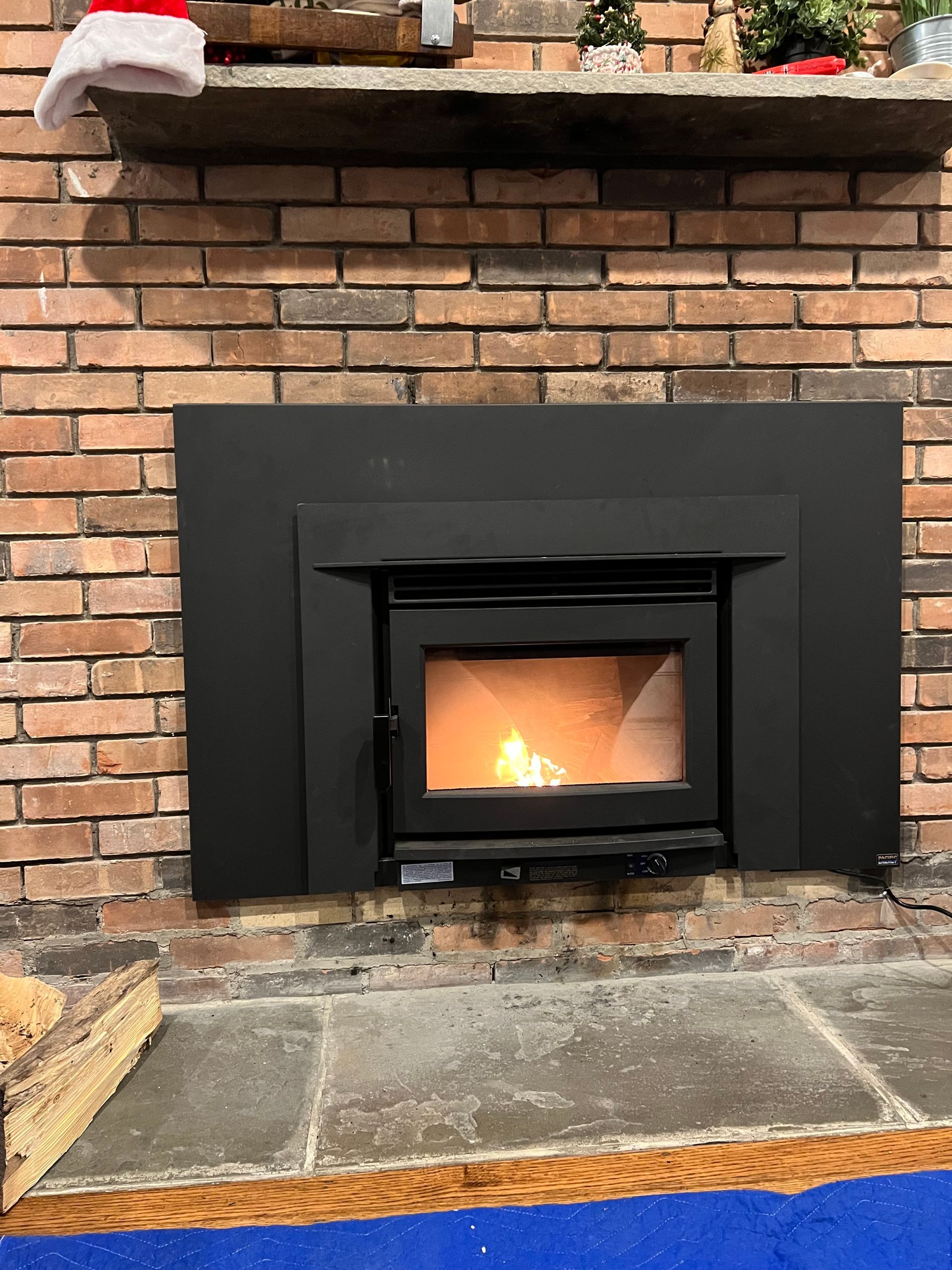 A black wood-burning fireplace insert with a glowing fire set into a brick chimney with a stone hearth.