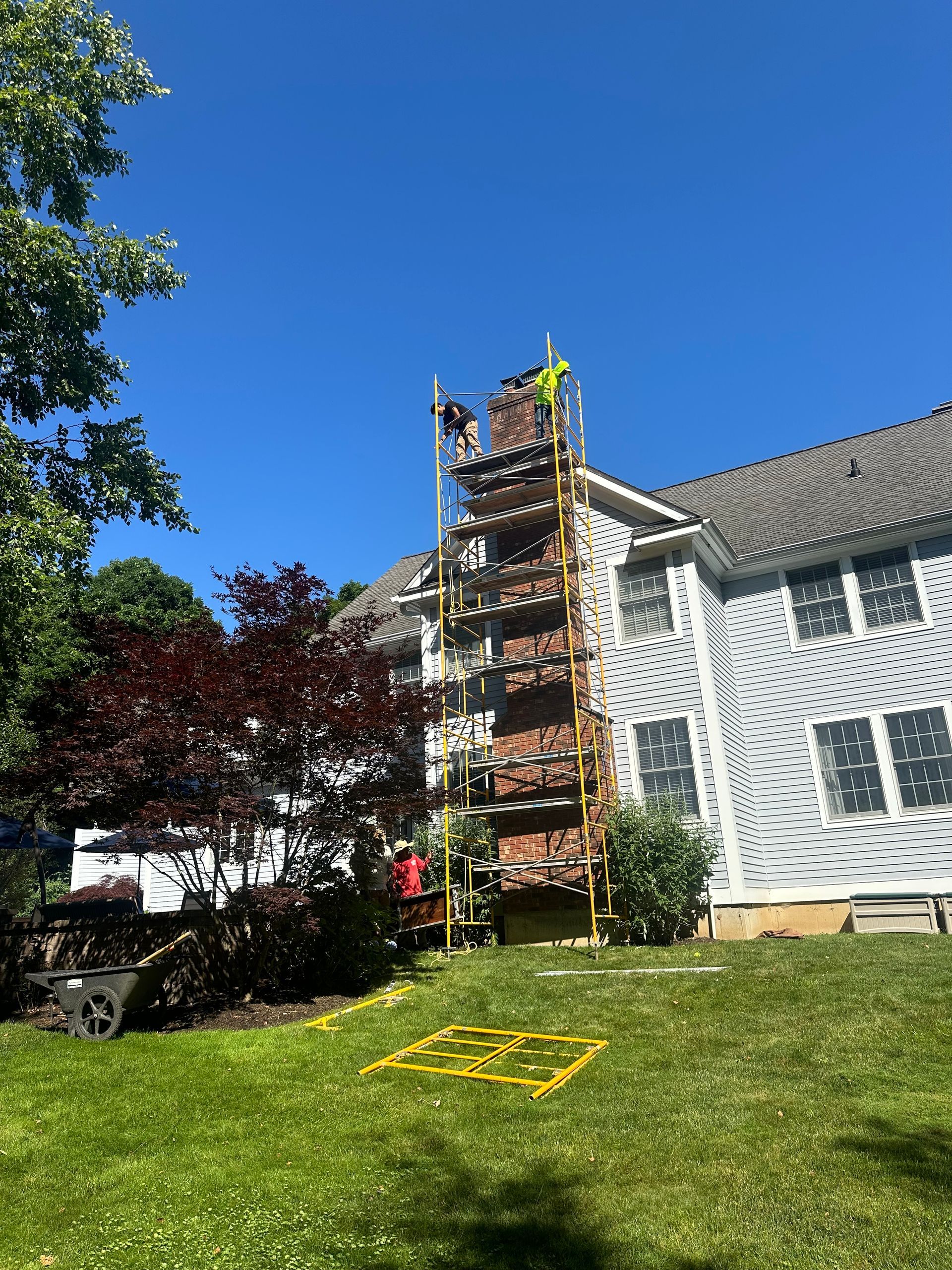 Workers on scaffolding repair a brick chimney on the exterior of a house under construction.