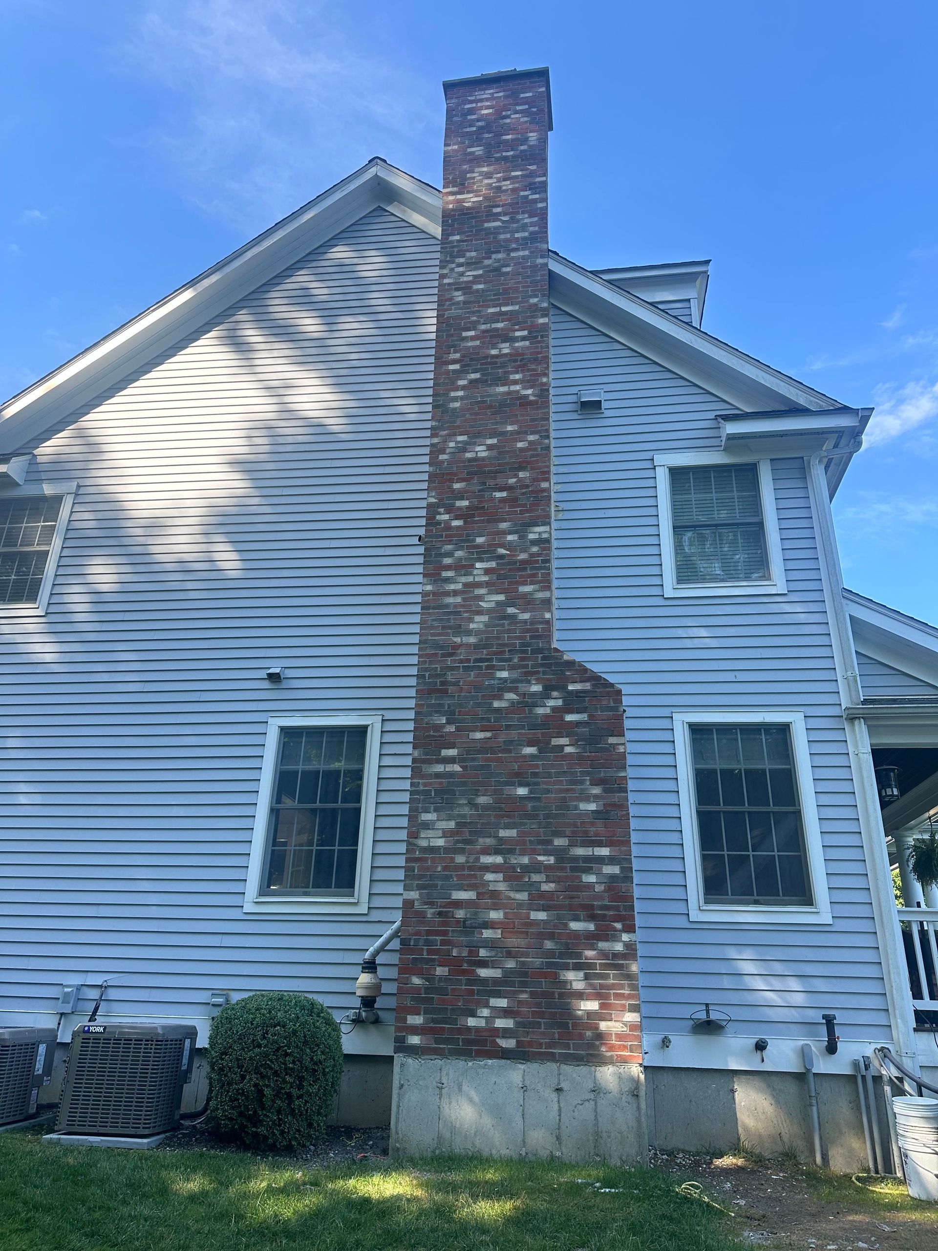 A light blue house with horizontal siding and a prominent, weathered brick chimney on a sunny day.