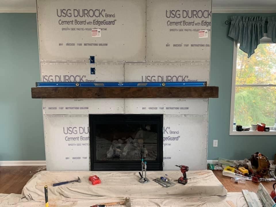 An unfinished fireplace surround under construction with cement board and a dark wood mantel installed in a living room.