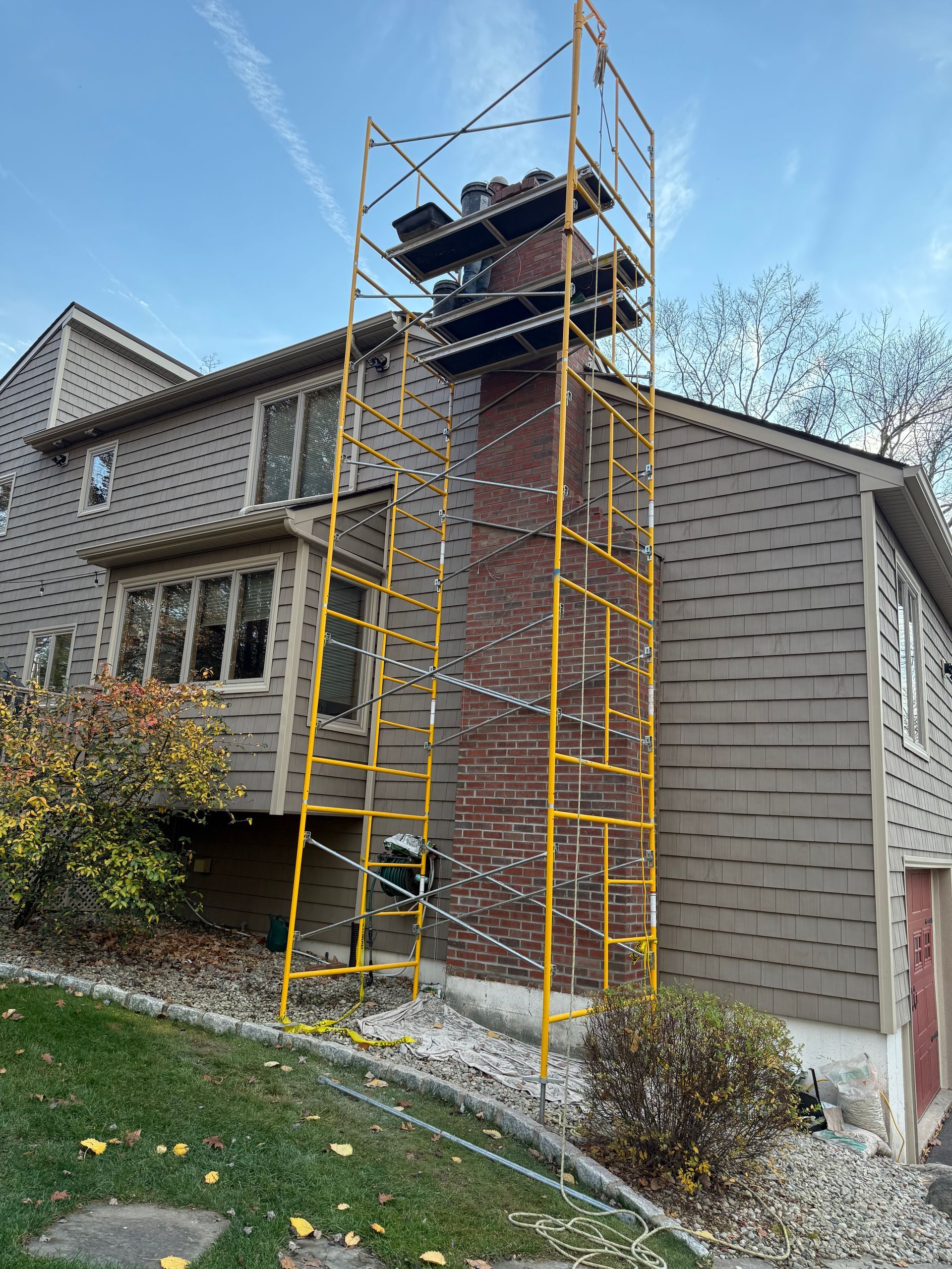 Yellow metal scaffolding standing against a brown shingled house to provide access to a brick chimney.